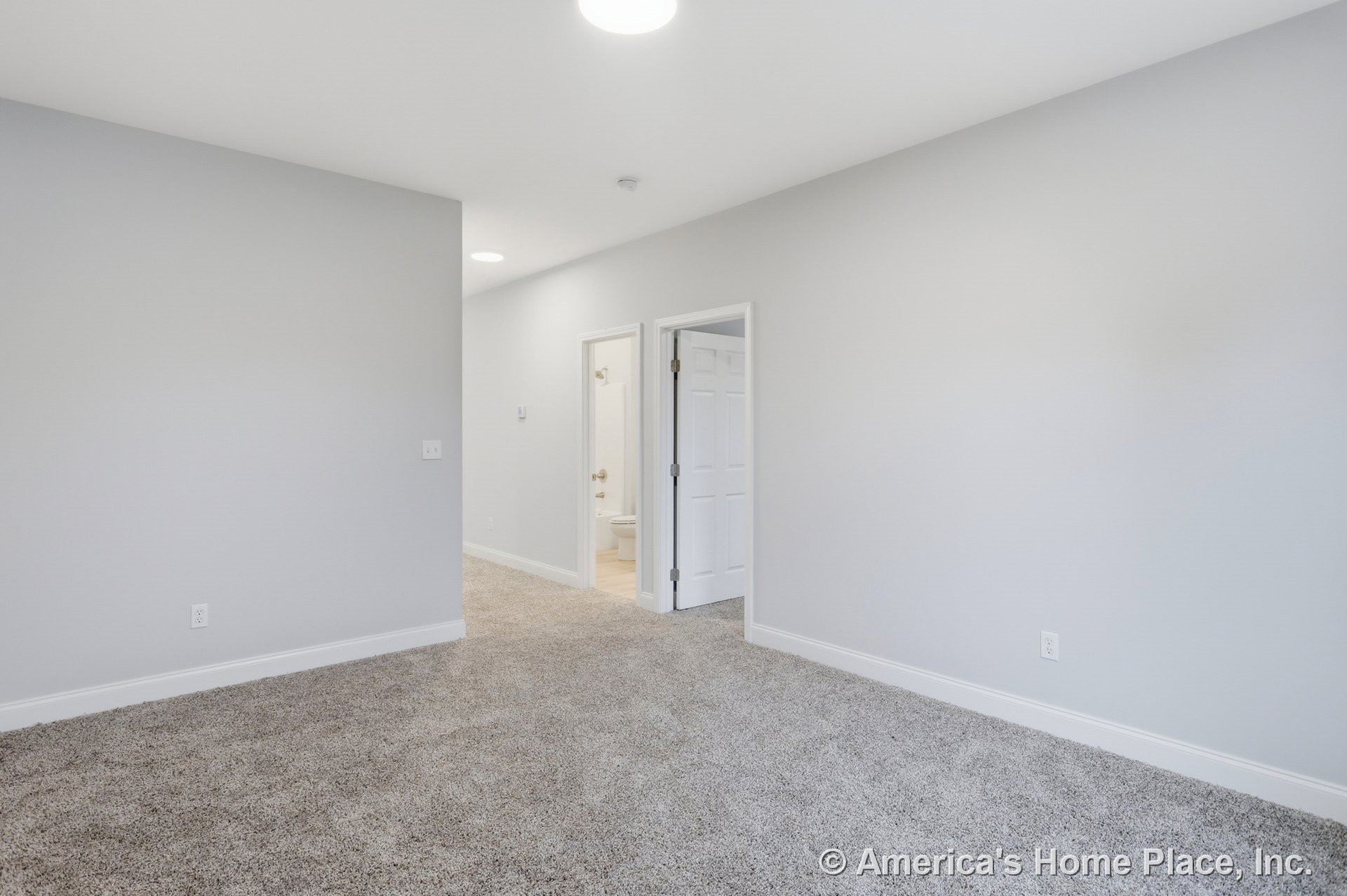 Bedroom with light gray walls, white baseboards and door trim, plush carpet flooring, recessed ceiling lighting, white paneled doors, and an adjoining bathroom featuring tile
