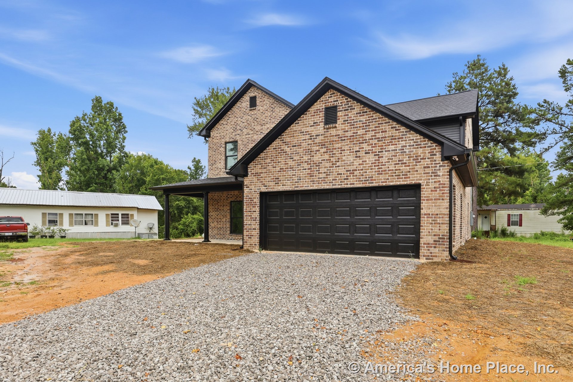 Brick exterior with black two-car garage door, covered front porch, gravel driveway, black trim, multi-pane windows, and modern entry door on a two-story home.