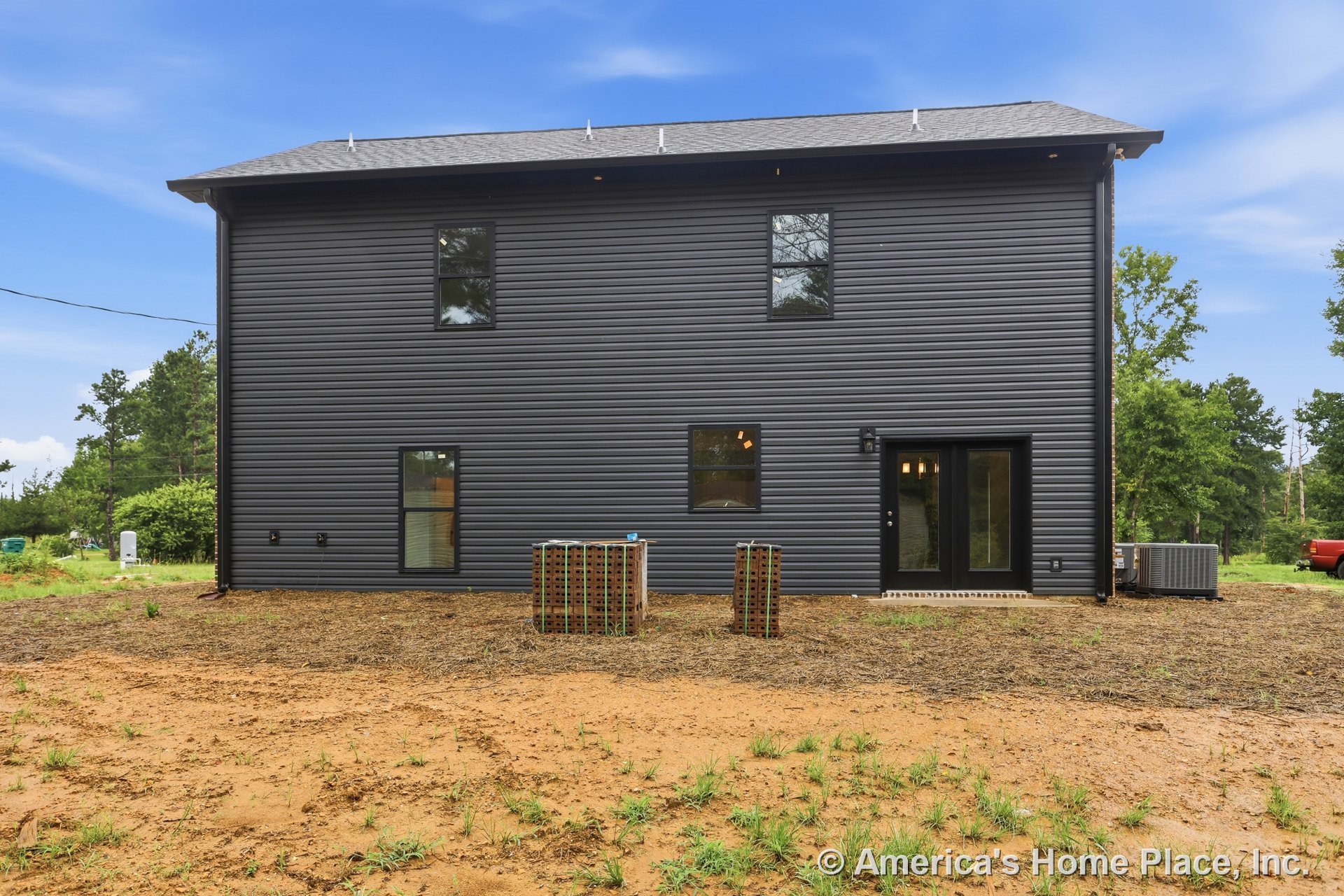 Dark horizontal siding with multiple rectangular windows, glass exterior door opening to backyard, roof with vents, outdoor HVAC unit, and modern trim detailing.