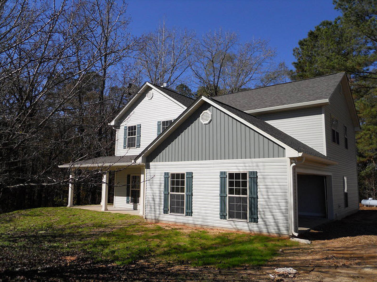 Two-story house with white siding, multi-pane windows, attached garage, manicured lawn, and mature trees in the background