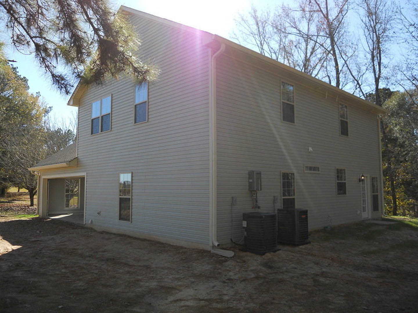 Modern two-story home with light siding, white-framed windows, attached garage, paved driveway, and landscaped front yard with trees.