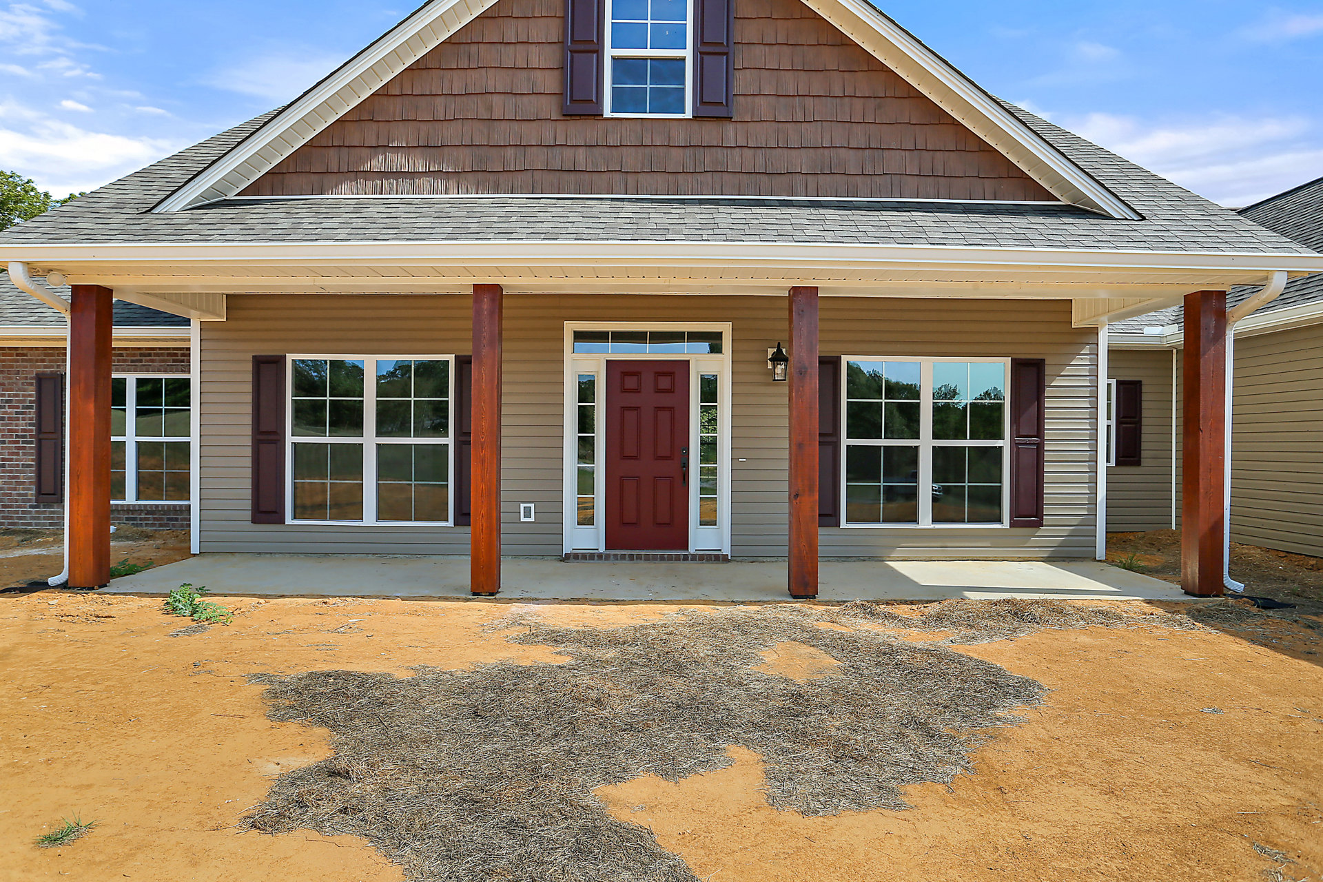 White siding house with a red door featuring glass panes and a white frame, gravel driveway, porch area, and windows with white frames and blue-tinted glass