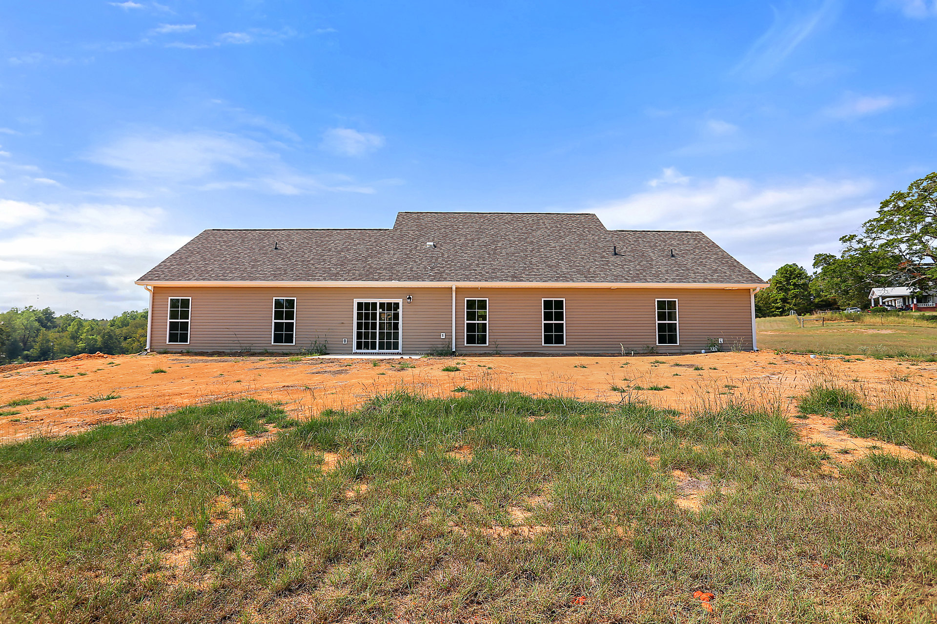 Modern house with white siding, black-trimmed sliding door, expansive green lawn, pile of dirt near trees, blue sky overhead