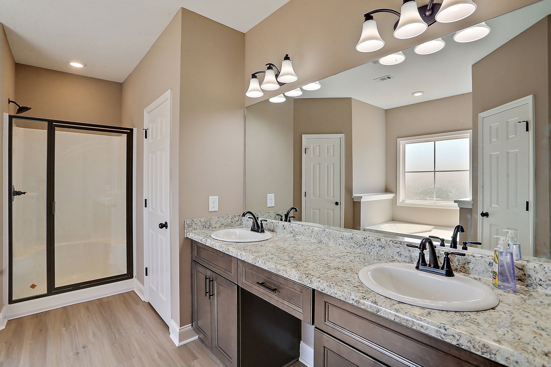 Bathroom with double vanity, wide frameless mirror, glass shower enclosure, white cabinetry, black hardware, frosted window, and countertop accessories.