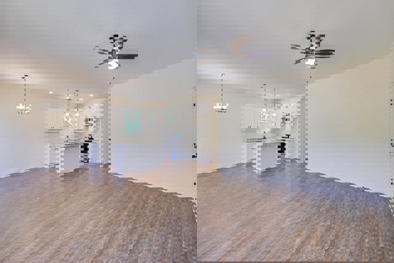 Spacious room featuring wood flooring, ceiling fan with light, white cabinets with black handles, white countertop and shelf, plaster walls, and modern light fixture.