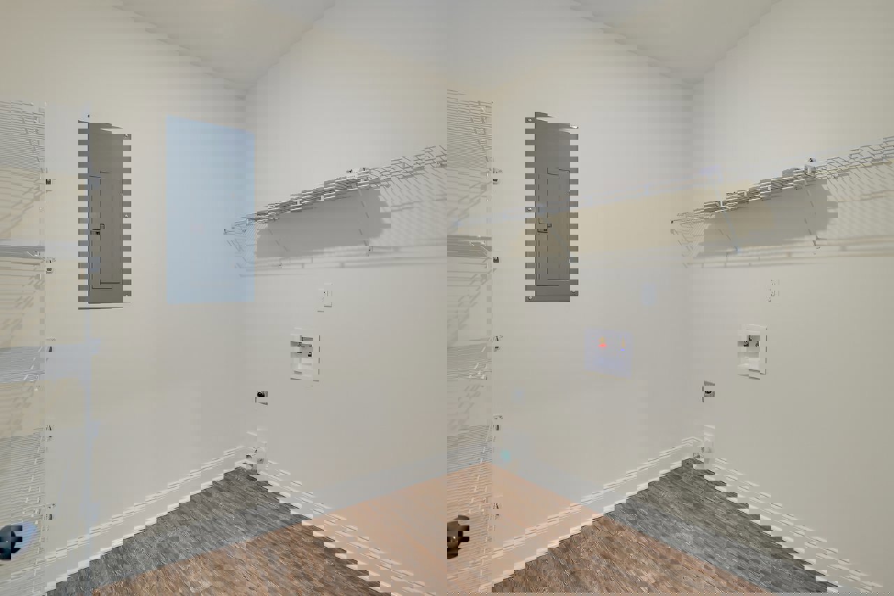 Wood floor room with metal shelving, grey door with lock, white shelving against white plaster wall, white box topped with red and blue items, blurry black object in foreground