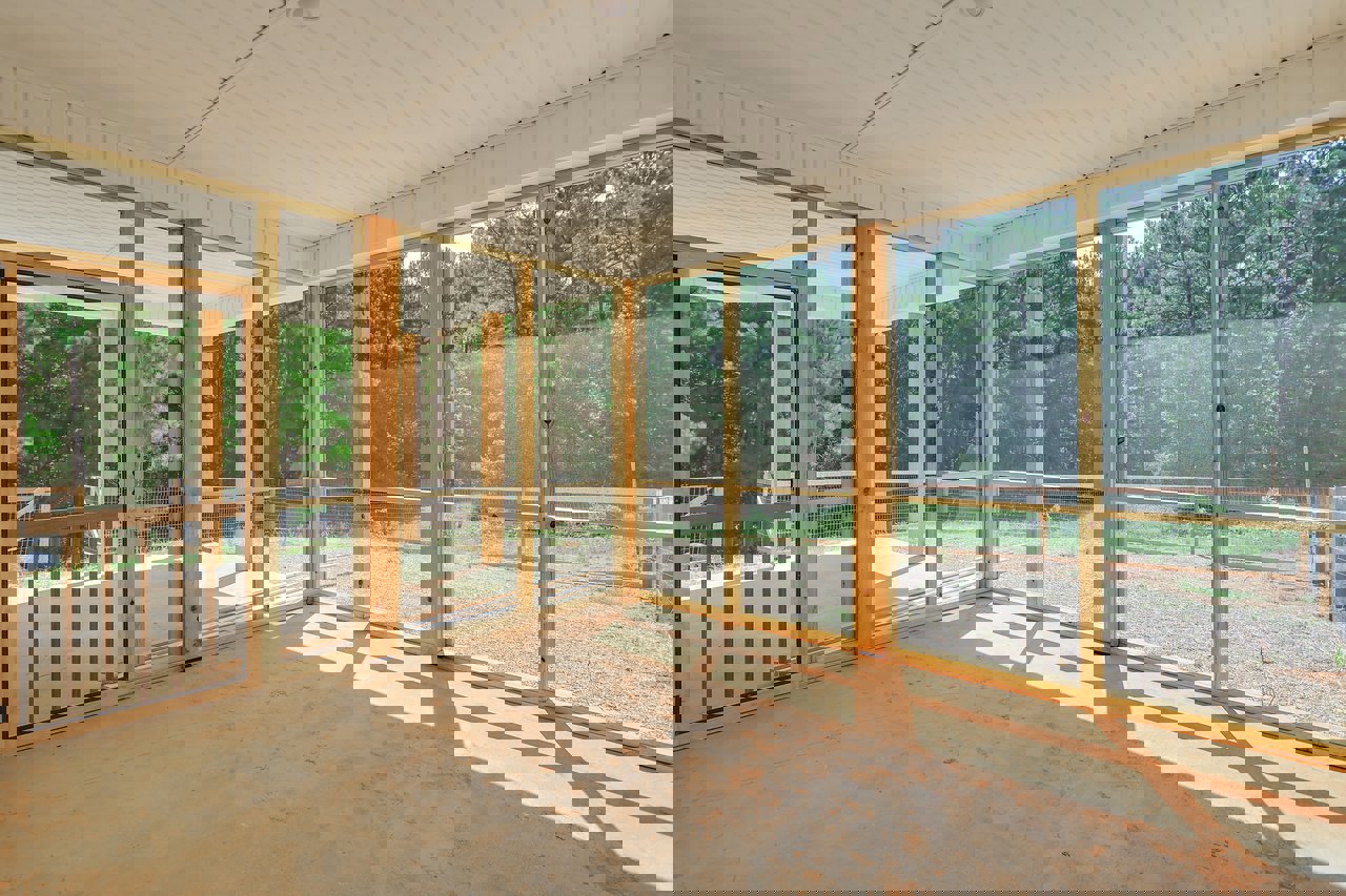 Modern room with floor-to-ceiling glass walls, white ceiling with recessed lighting, wooden floor, and view of porch and wooden fence through large windows