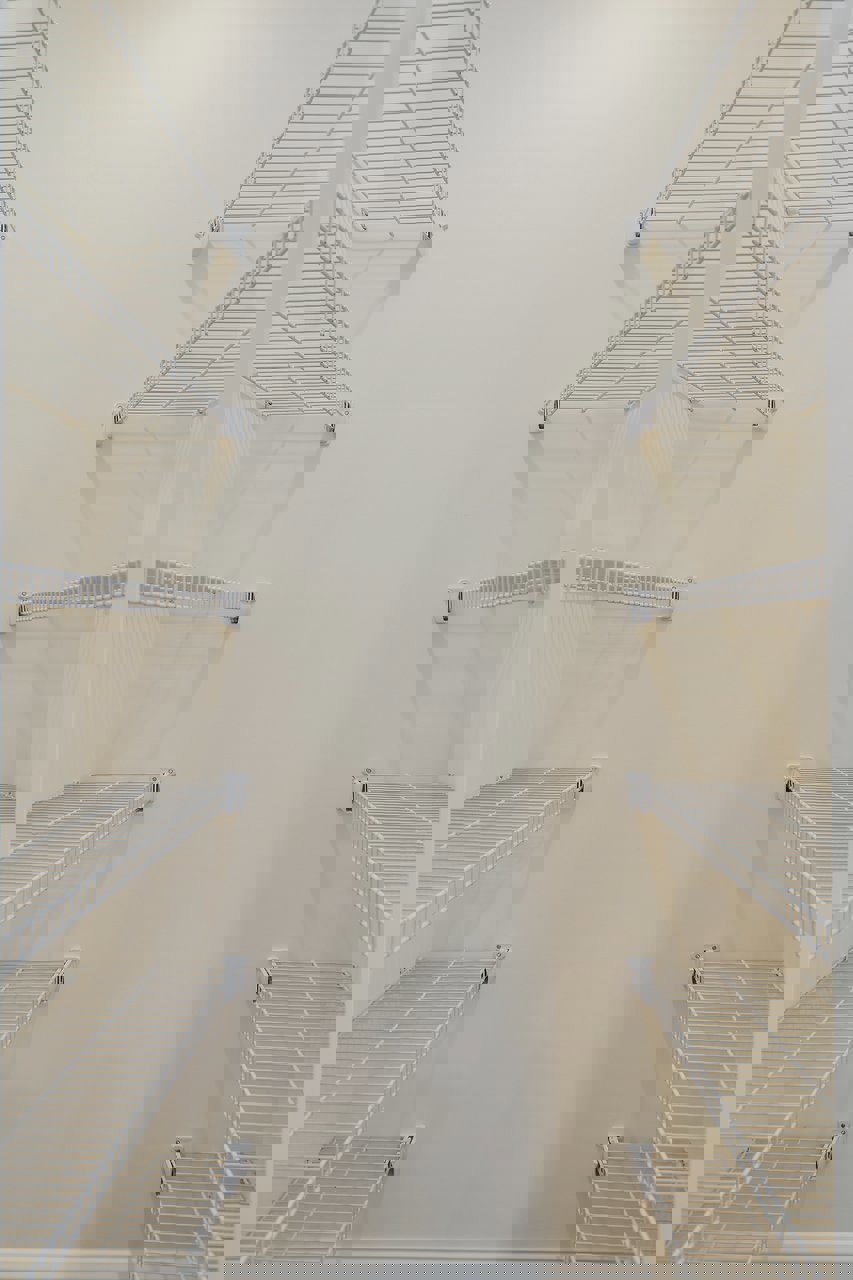 White wire shelving mounted on a wall in a room with a smooth ceiling and neutral painted walls.