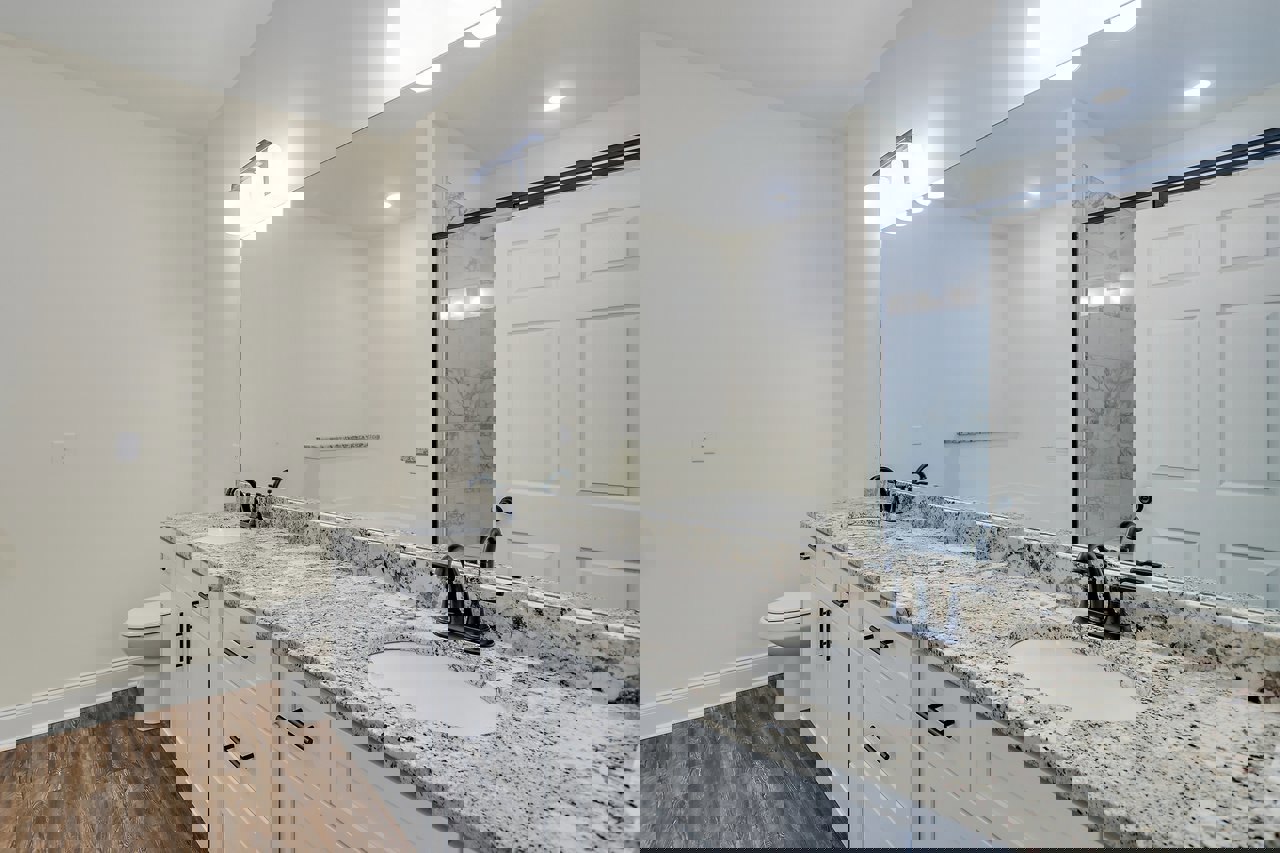 Marble countertop with white undermount sink and black faucet, large wall mirror above, white toilet with closed lid, white door, light tile flooring