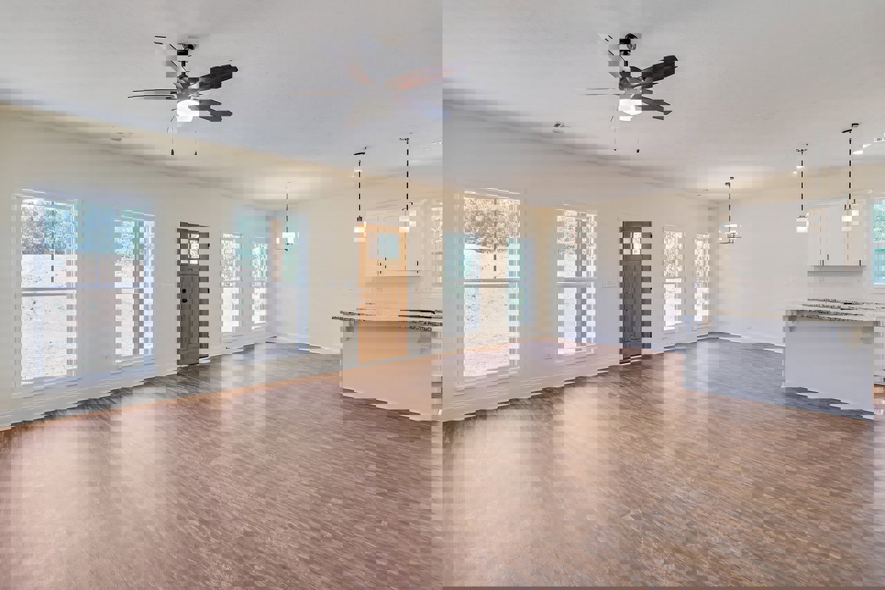 Open room with light wood flooring, white walls, ceiling fan with light fixture, marble-topped surface, large window overlooking grassy field, and paneled door.