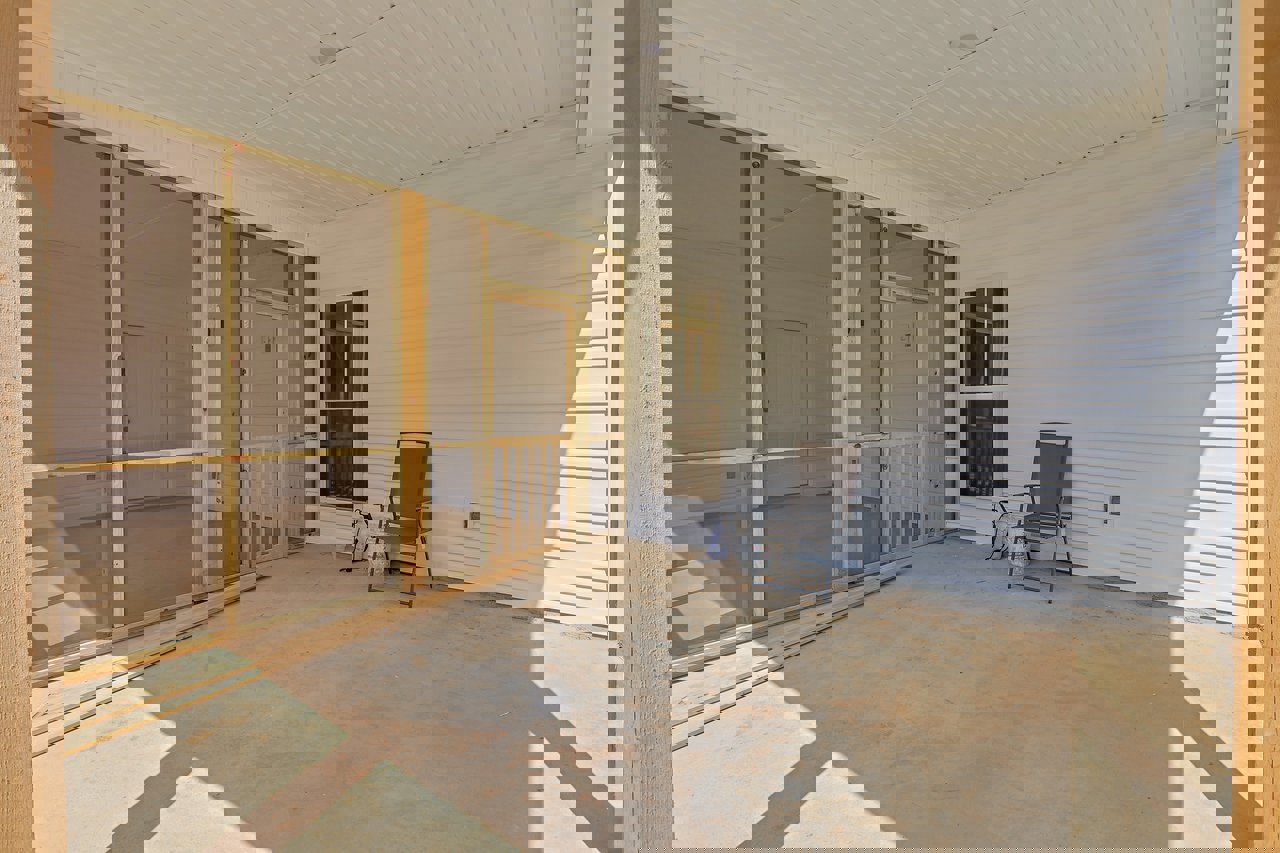 Screen door with white trim on a covered porch, concrete floor, wooden chair, and partial view of window and fence