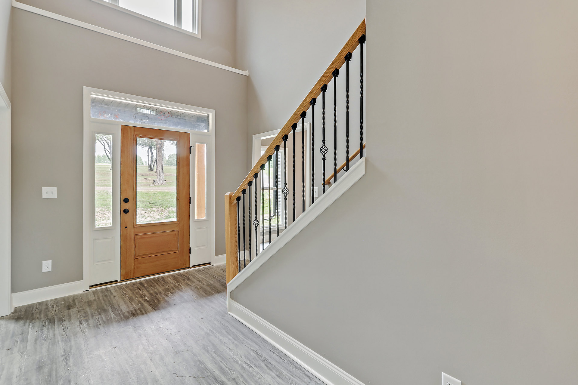 Wooden staircase with matching handrail and balusters, adjacent to a glass-paneled door overlooking grassy yard and trees, plaster walls, and window framing tree trunk and lawn.