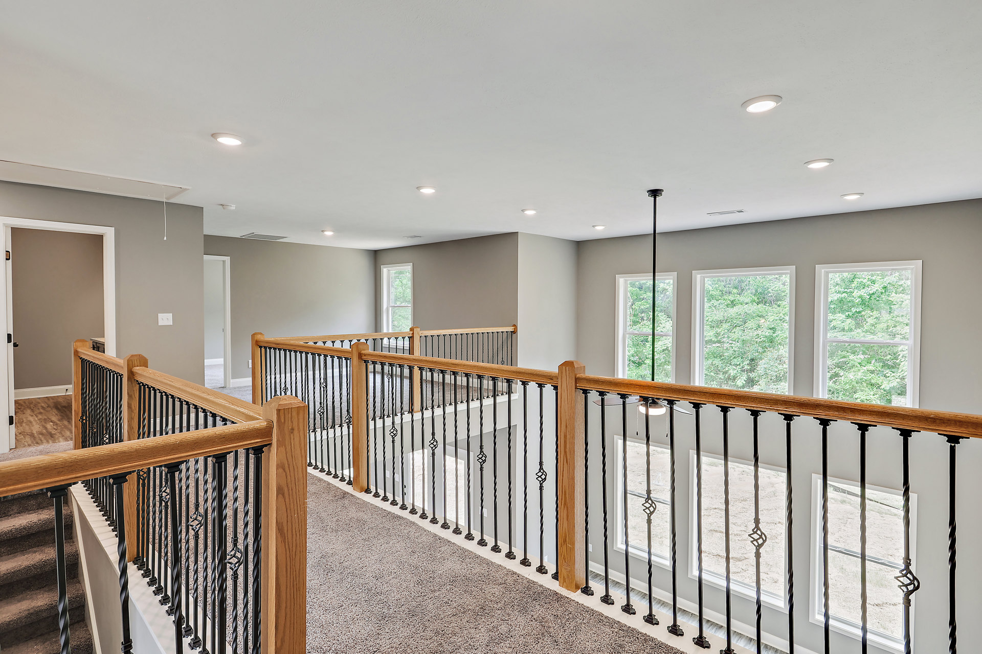Wood staircase with slender railing, large windows framing leafy trees, white walls, and light hardwood flooring