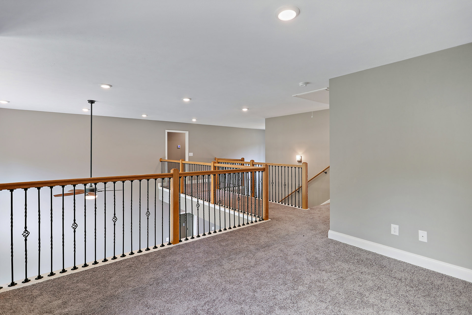 Wood staircase with black metal railing, white plaster walls, light fixture overhead, ceiling fan, and white door with decorative black accents