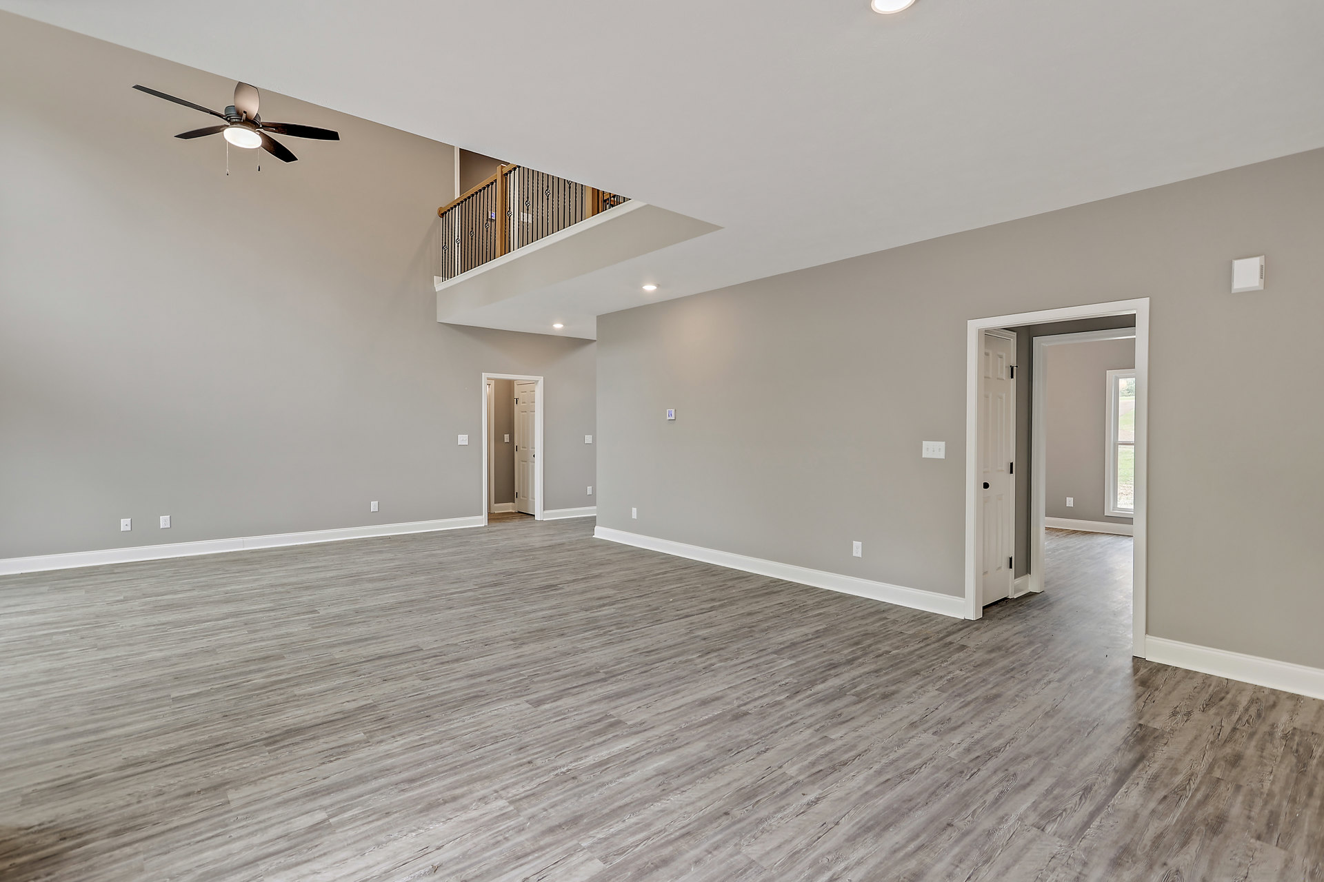 Spacious room with wood flooring, white plaster walls, ceiling fan with light, staircase featuring wooden steps and railing, and a door with nearby light switch