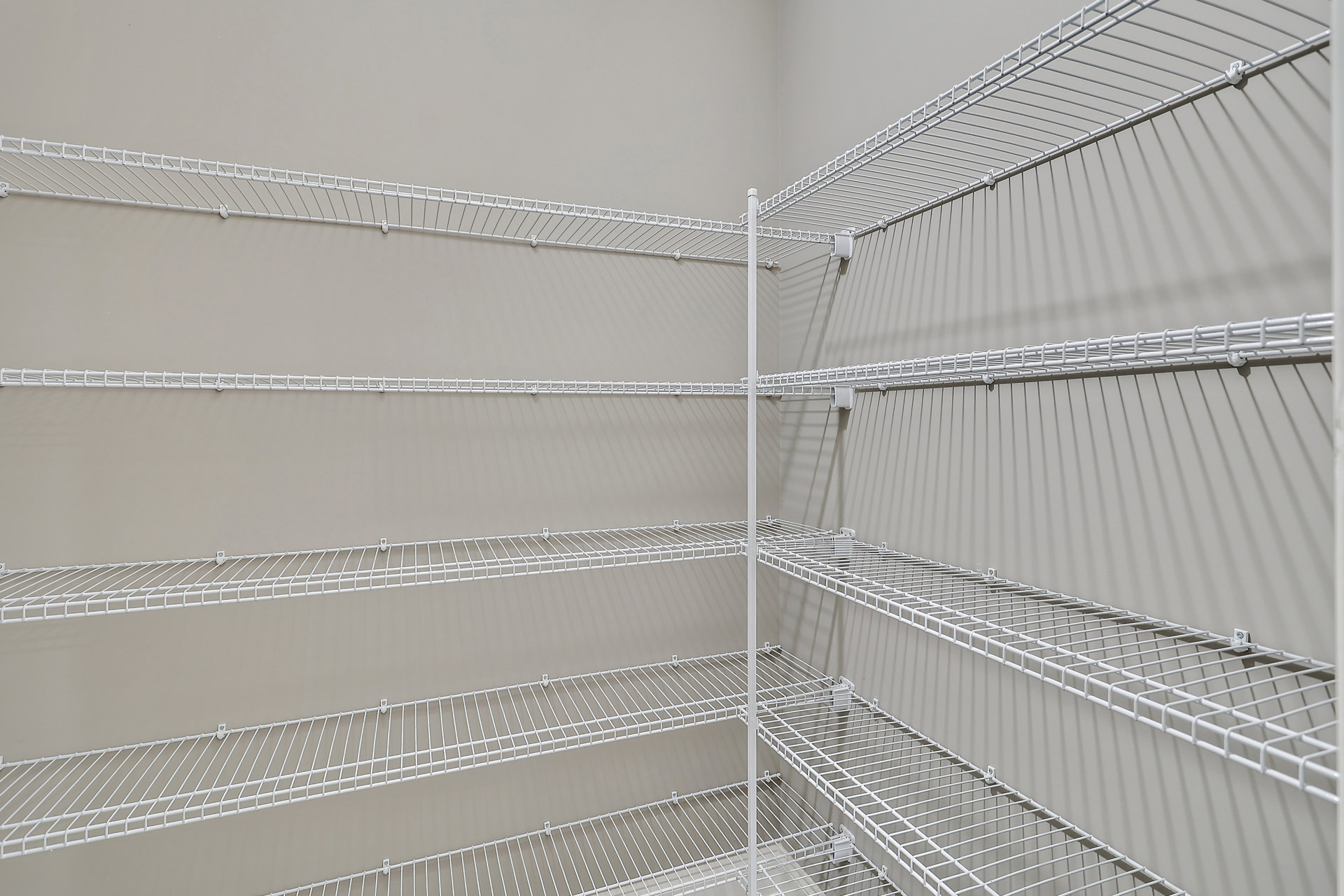 White wire shelving mounted on a wall in a closet with steel supports