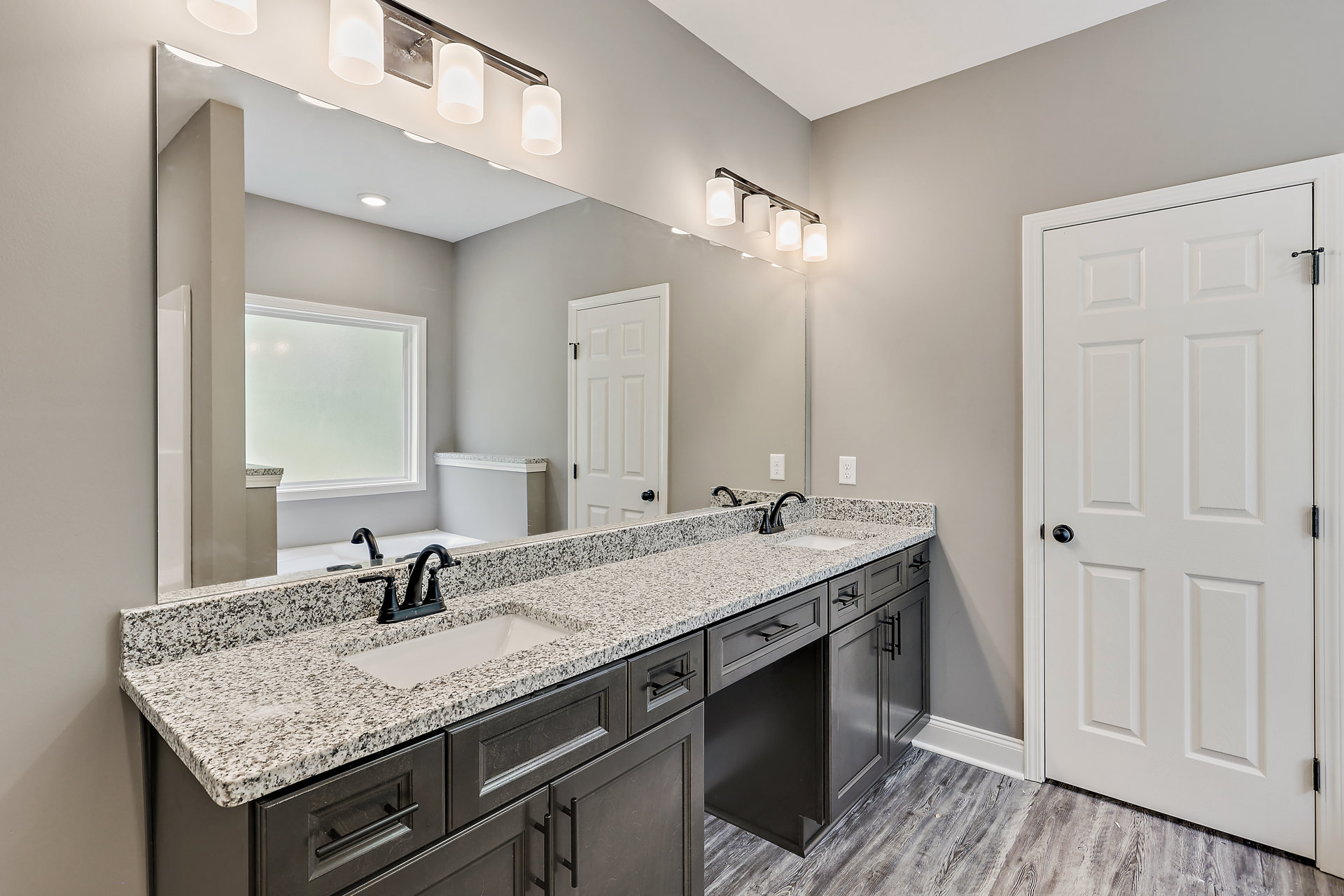 Marble countertop bathroom with undermount sink, white cabinetry, black hardware, white door, and window above the counter.