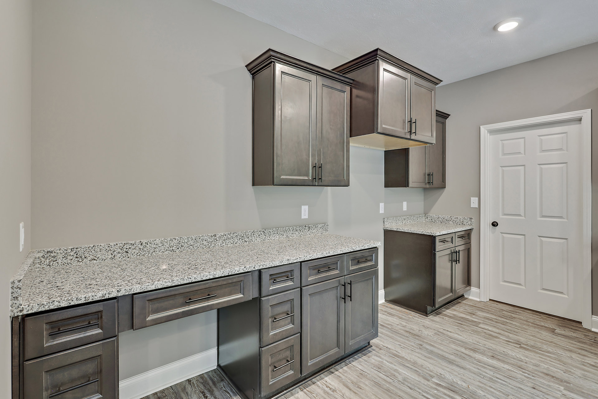 Granite kitchen countertops with grey cabinets featuring black handles, white door with black hardware, stainless steel sink, and built-in appliances.