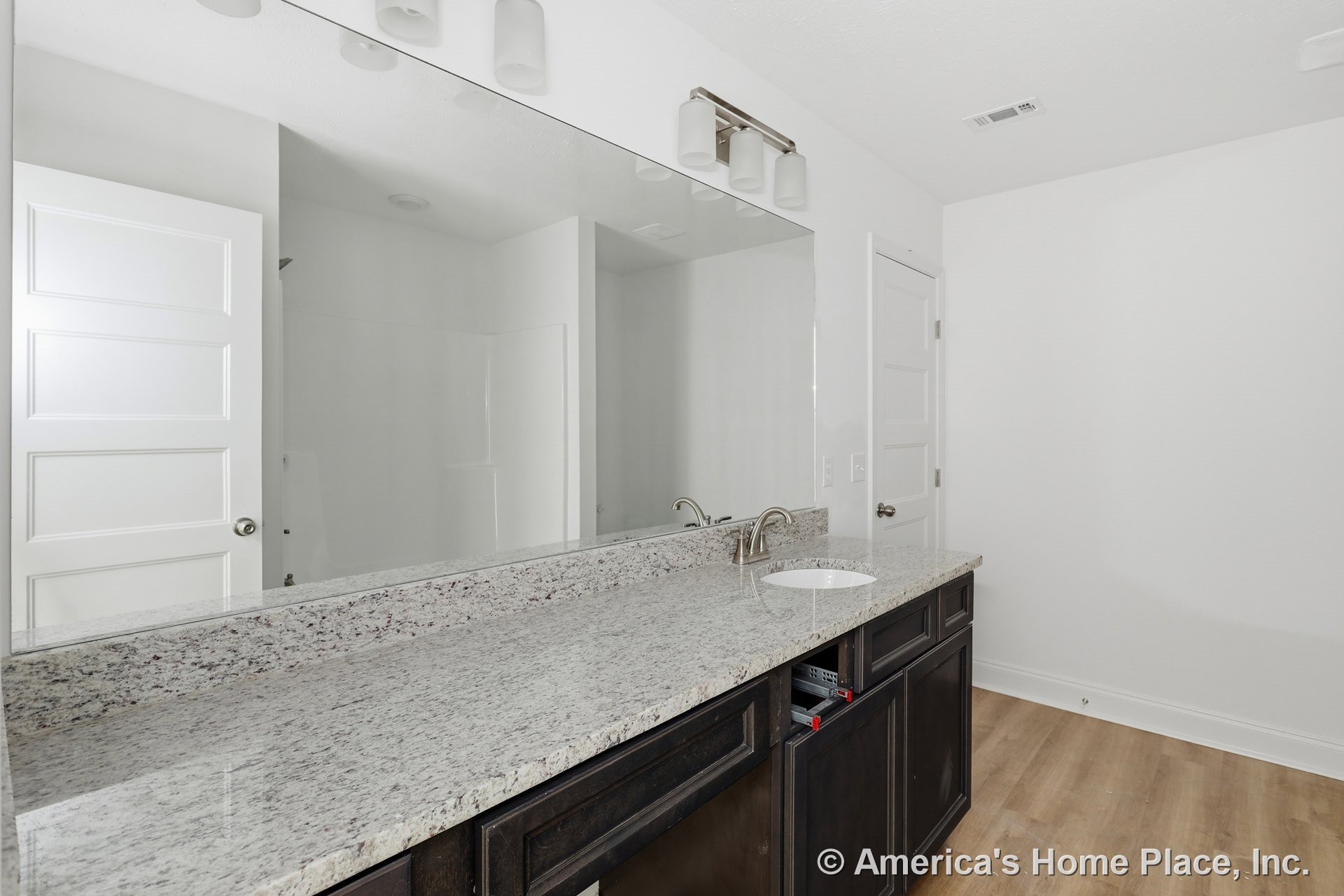Granite vanity top with single undermount sink, dark wood cabinetry, wide wall-mounted mirror, modern light fixture, and white paneled doors in a contemporary bathroom.