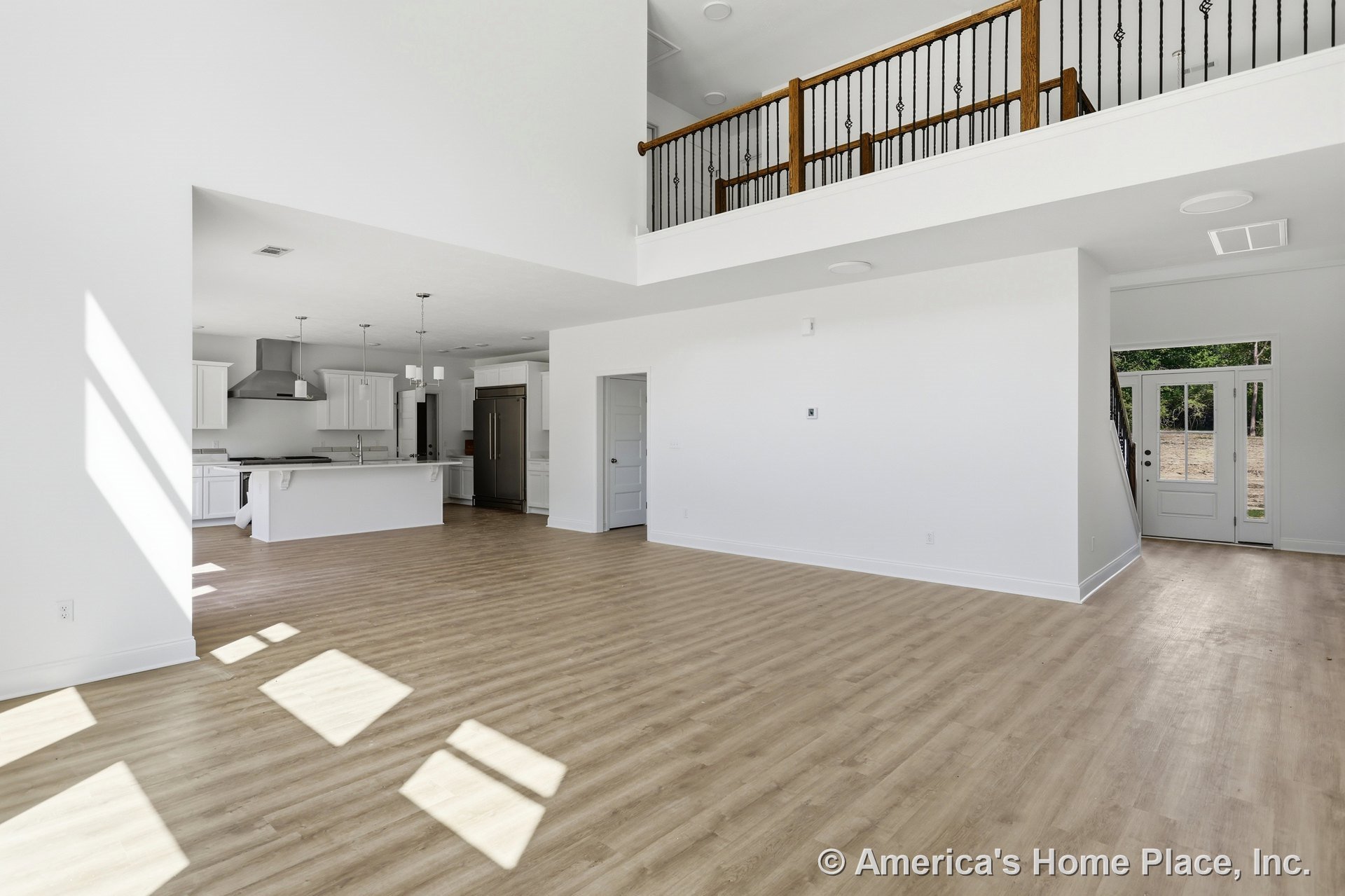 Open-concept living area with light wood flooring, modern kitchen featuring white cabinetry, stainless steel range hood, kitchen island with pendant lighting, loft with iron