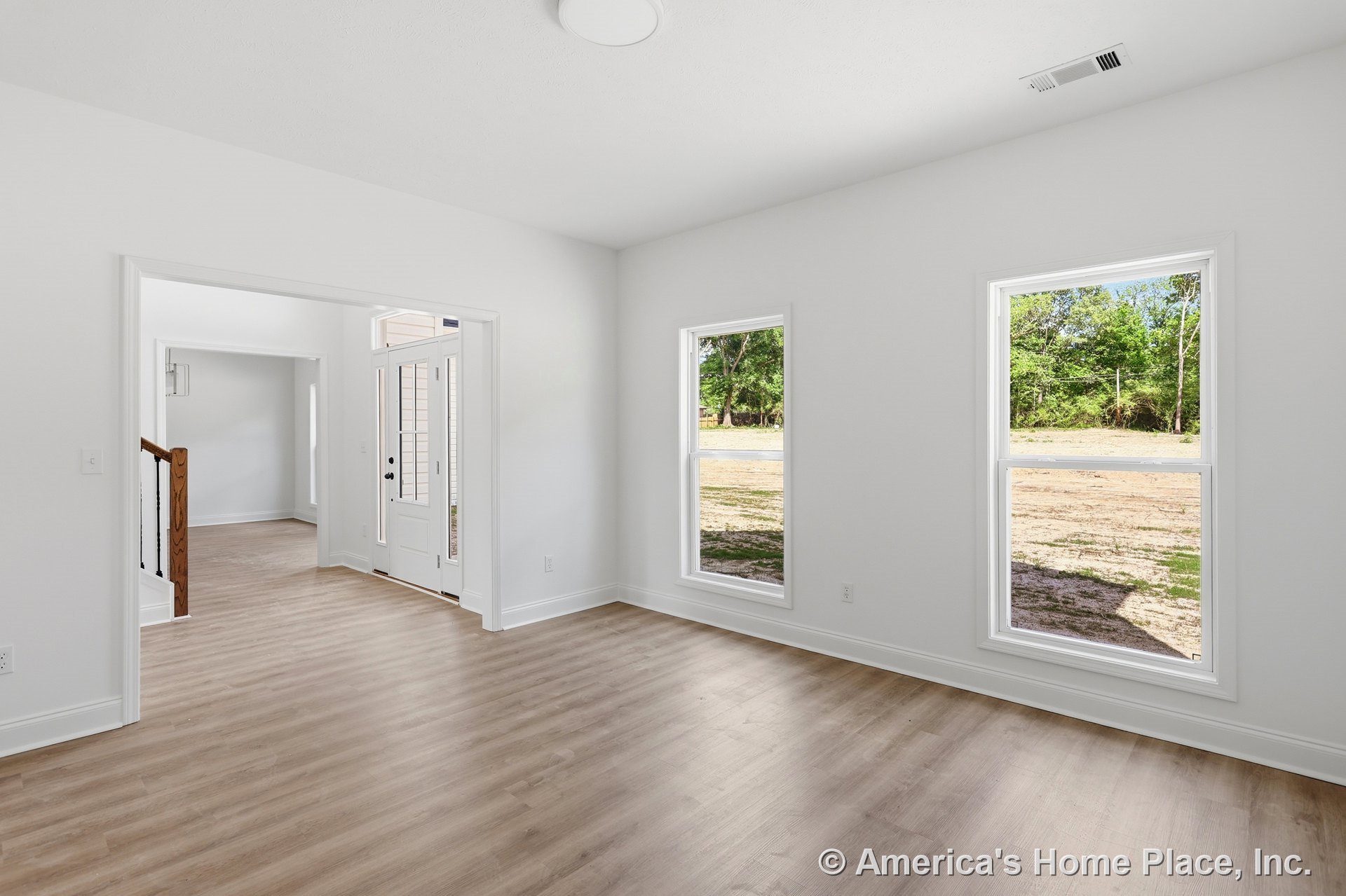 Foyer with double windows framed in white trim, light wood plank flooring, white walls and ceiling, glass-paneled front door, wood stair railing detail, and baseboards in an open