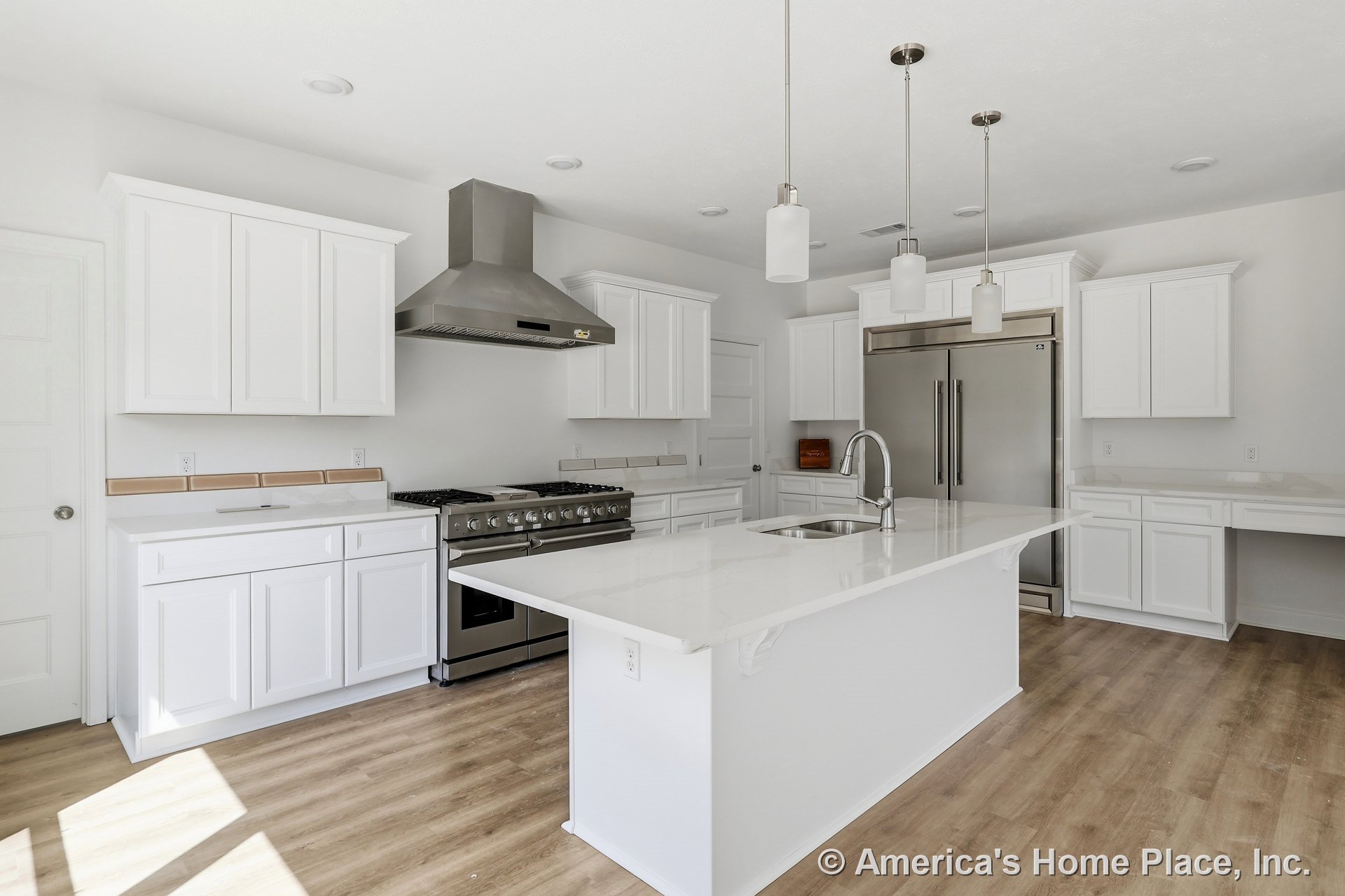 Spacious kitchen with large island featuring undermount sink, white shaker cabinets, quartz countertops, stainless steel range and hood, built-in refrigerator, pendant lighting