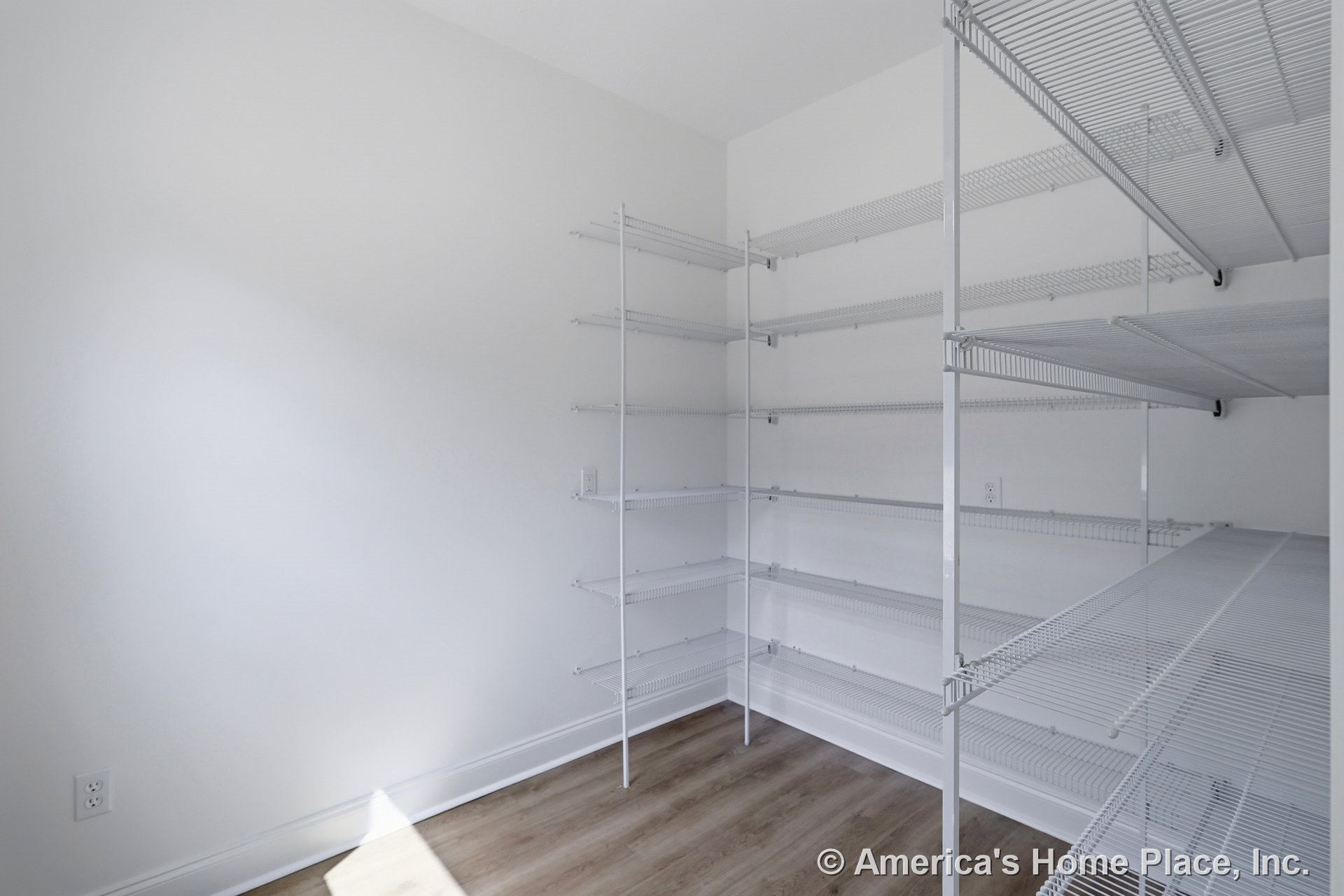Walk-in pantry with built-in white wire shelving, light wood-look flooring, white walls, baseboard trim, and visible electrical outlets.
