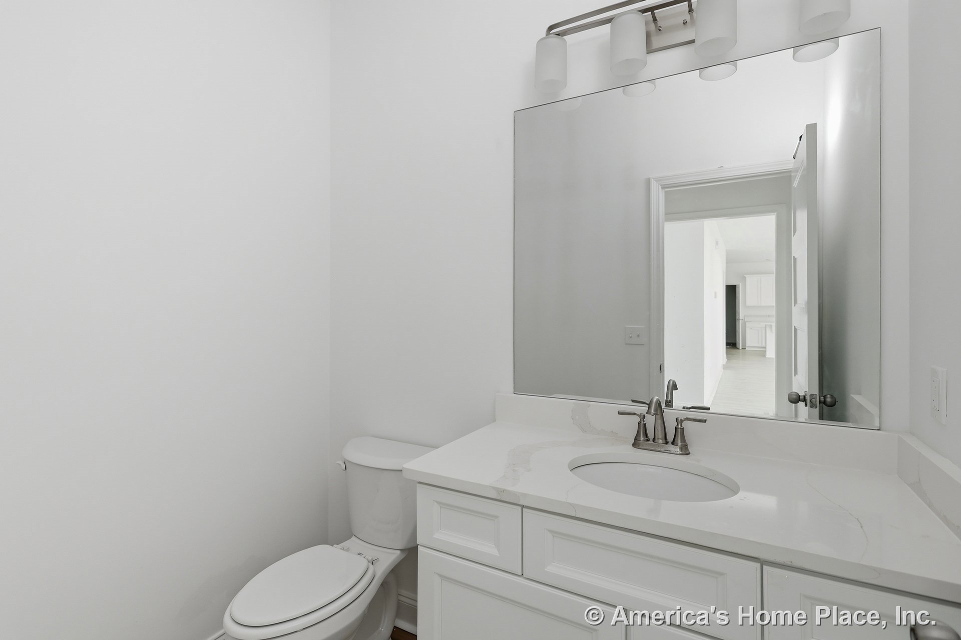 White shaker vanity with marble-look quartz countertop, large frameless wall mirror, chrome faucet, wall-mounted vanity light, and white toilet with modern trim.