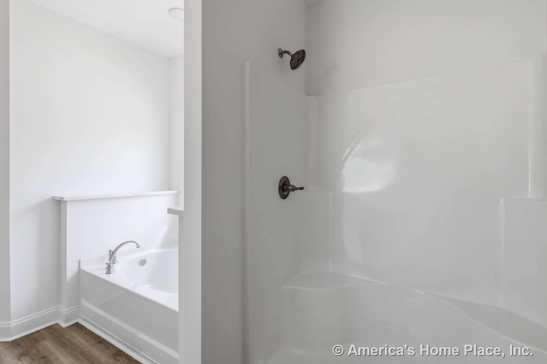 Built-in white acrylic shower enclosure beside a separate soaking tub with chrome faucet, wood-look flooring, white walls and trim, and recessed ceiling lighting.