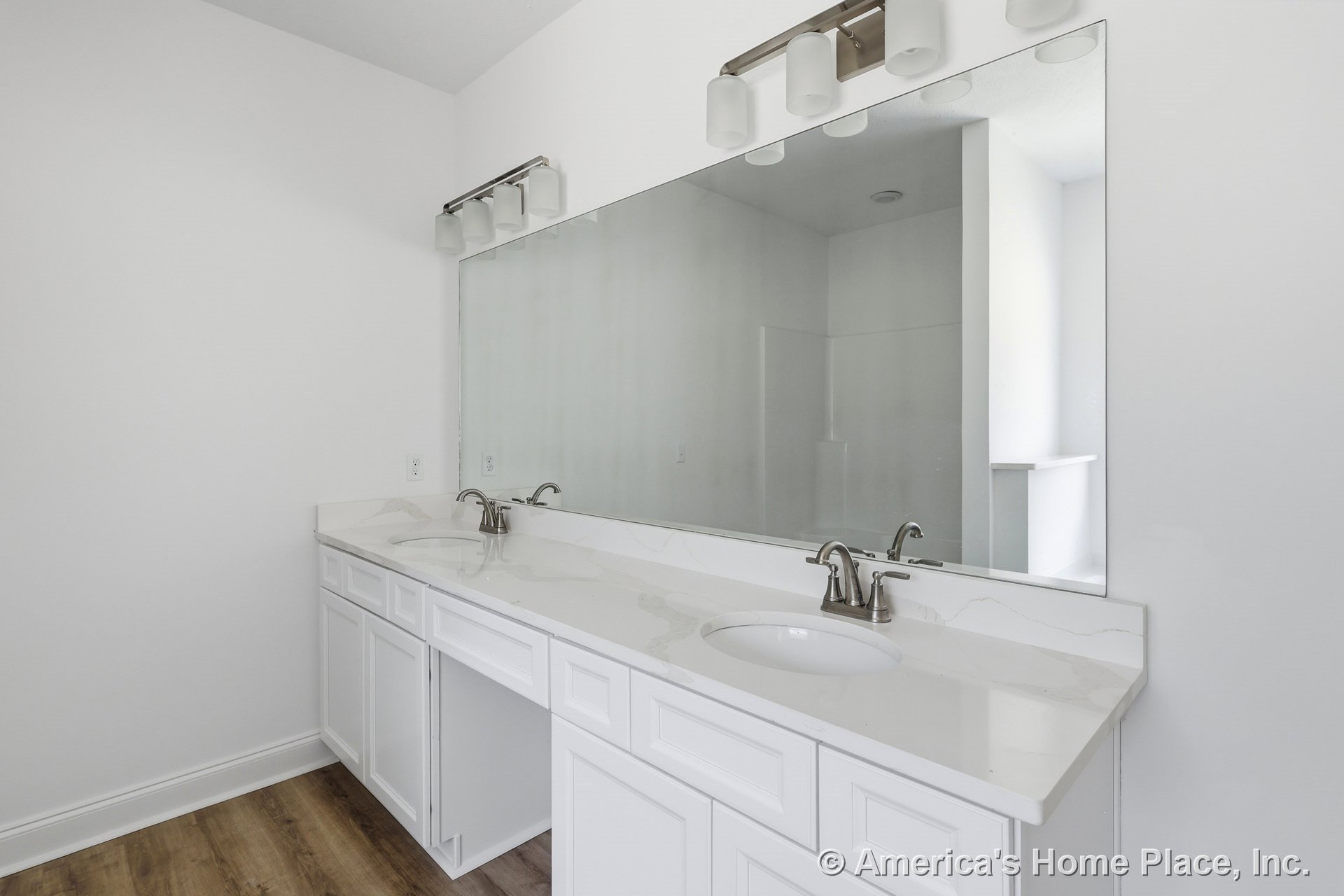 Double vanity with white shaker cabinets, marble-look countertop, undermount sinks, chrome faucets, large wall mirror, built-in overhead lighting, and wood-look flooring.