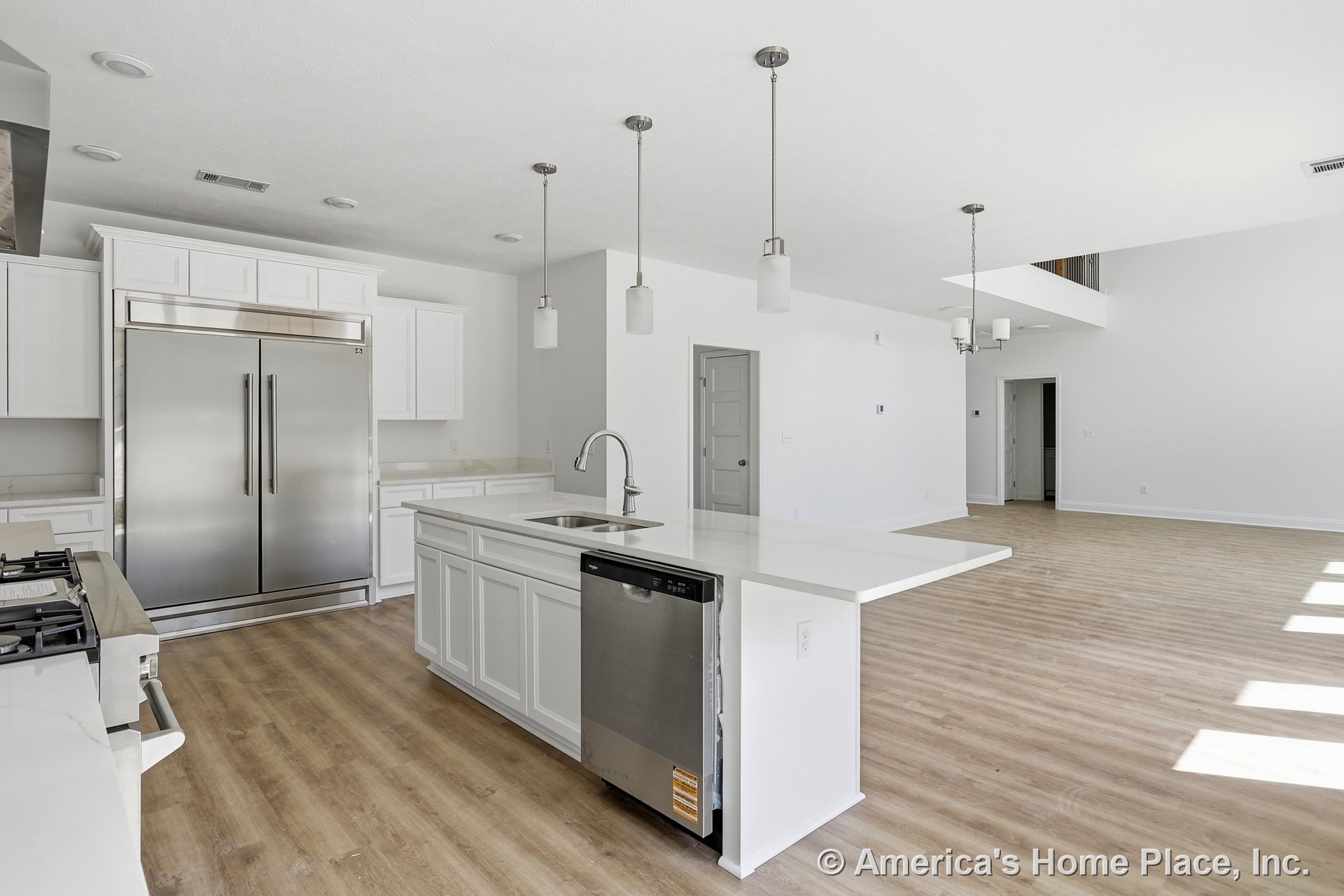 Open concept kitchen with white shaker cabinets, quartz countertops, center island featuring a built-in sink and dishwasher, stainless steel refrigerator, pendant and recessed
