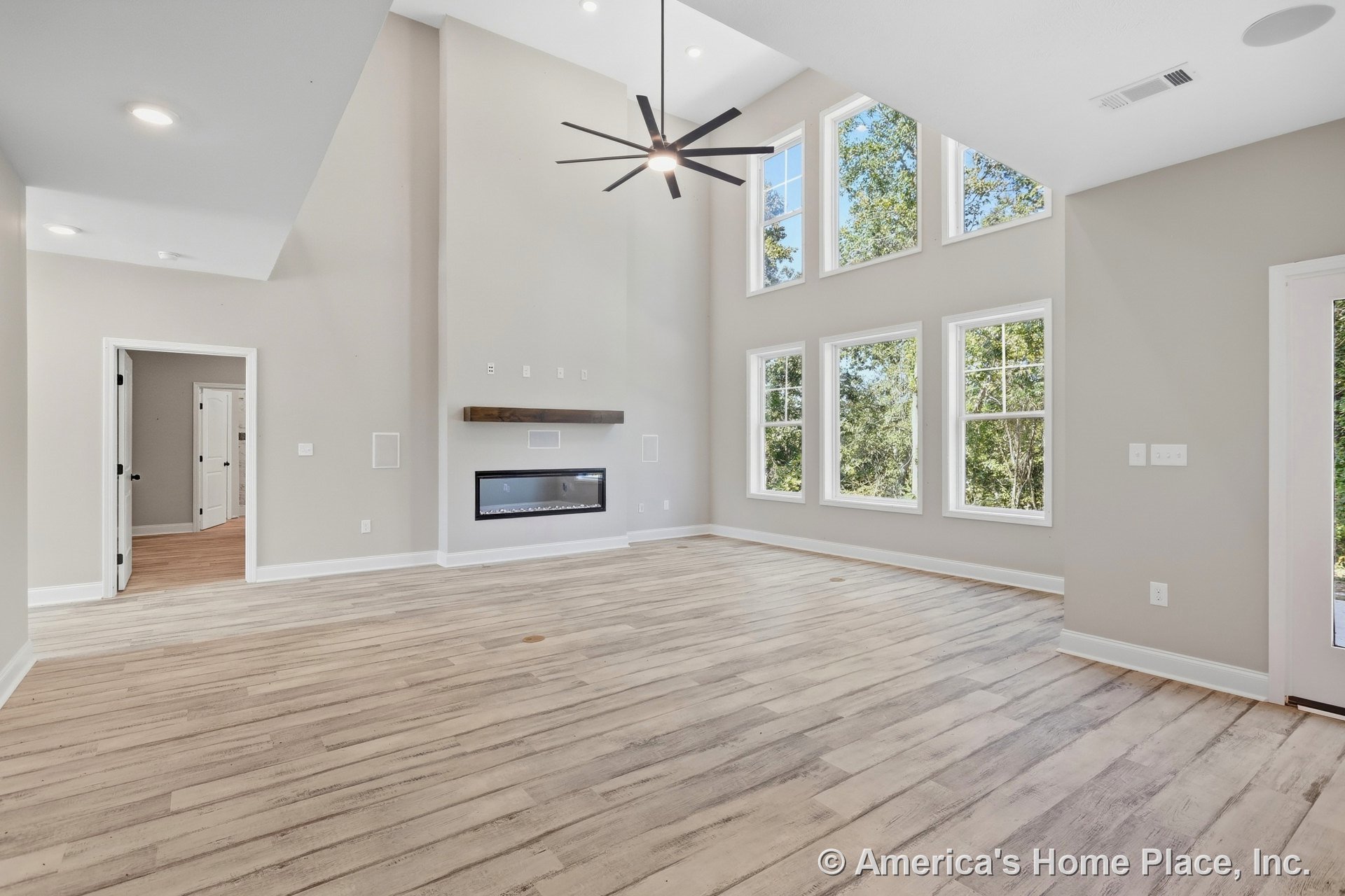 Double-height living room with expansive grid windows, modern linear fireplace set in neutral walls, light wood plank flooring, recessed lighting, contemporary ceiling fan, and