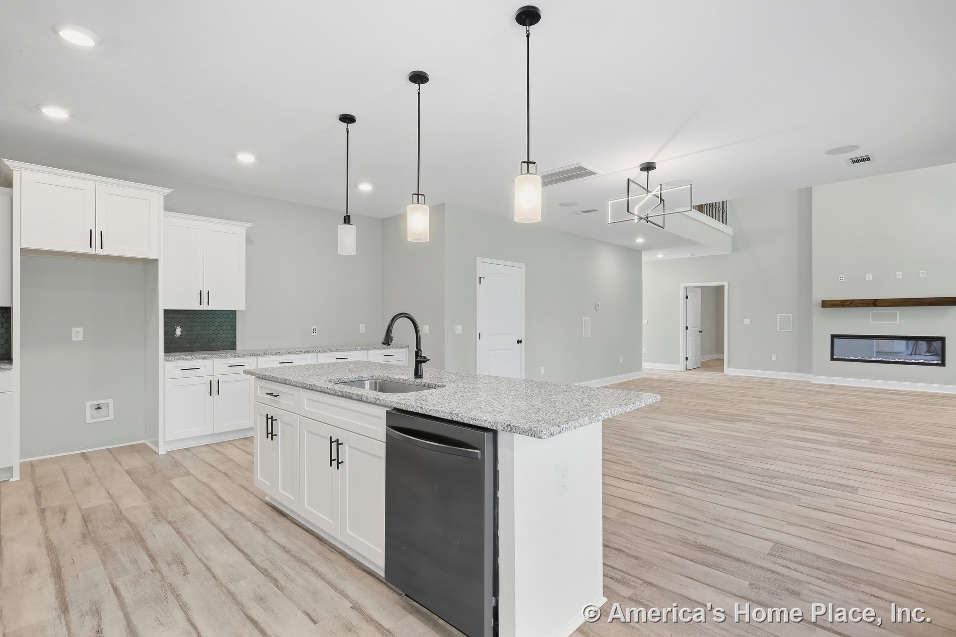 Open kitchen with white shaker cabinets, granite island, black hardware, pendant lights, wide plank wood flooring, and a linear fireplace with wood mantel in a spacious open floor