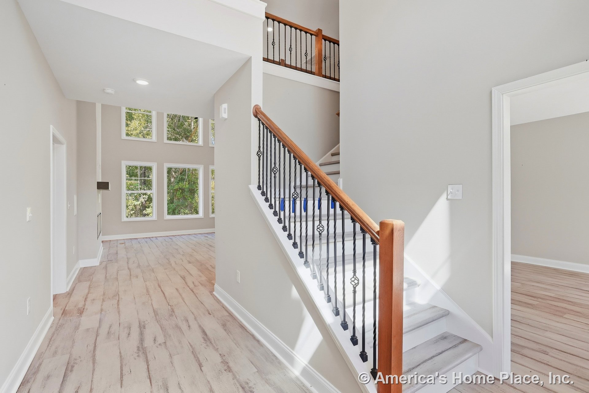 Foyer with iron stair balusters and wood handrail, light wood flooring, white trim and baseboards, open layout leading to living area with large window wall, high ceiling, and