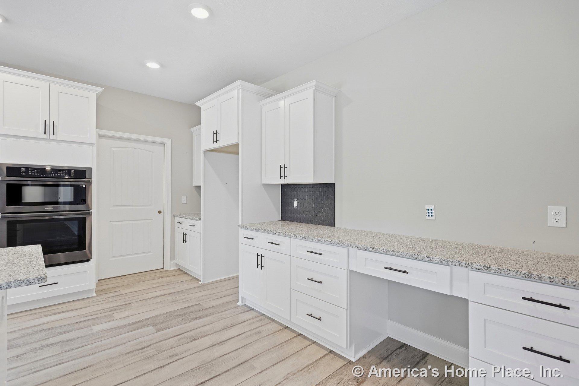 White shaker cabinets with granite countertops, black hexagonal tile backsplash, double wall ovens, recessed ceiling lights, light wood plank flooring, built-in pantry door, and