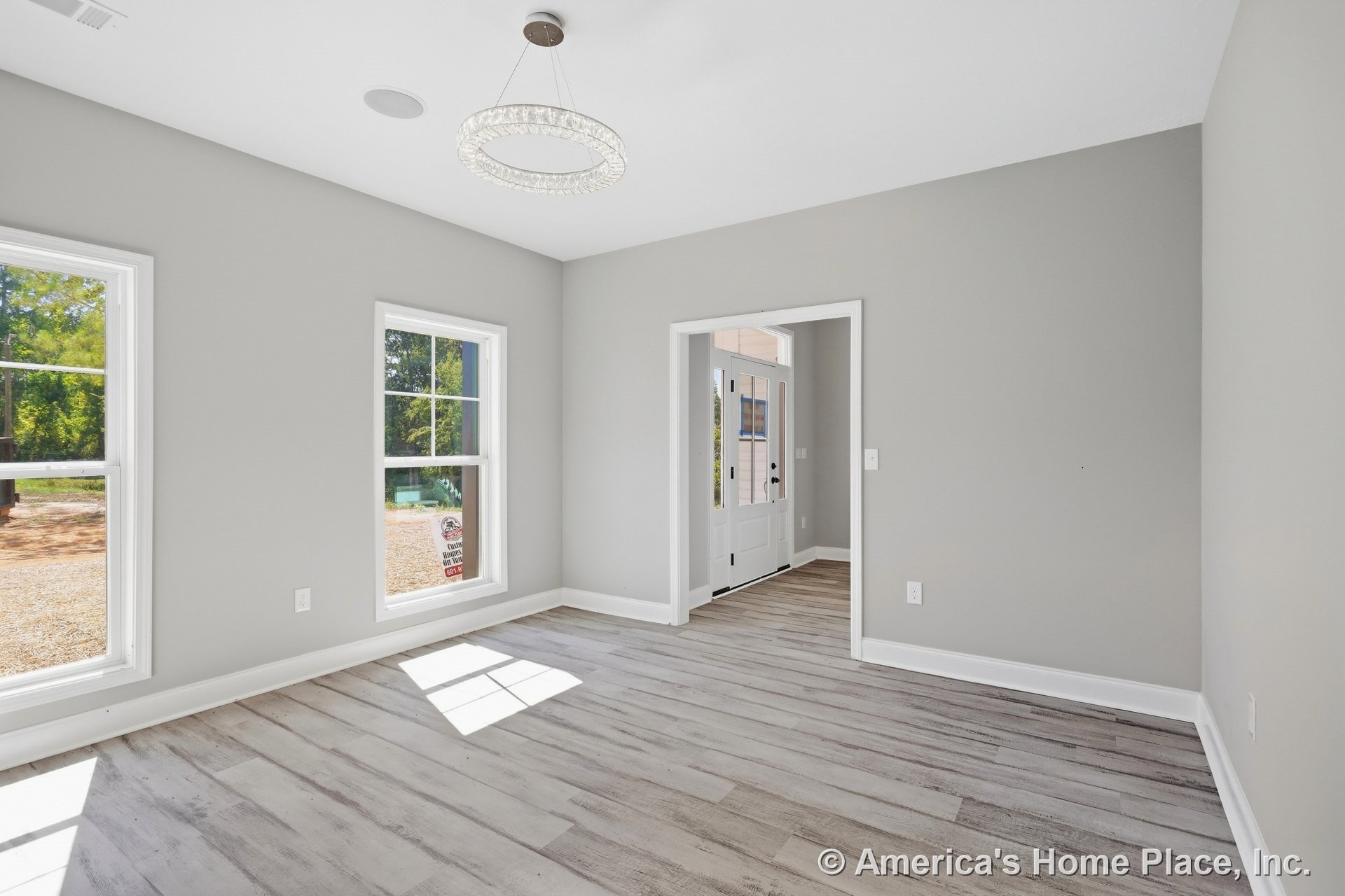 Bright foyer with light wood-look plank flooring, gray painted walls, large double-hung windows, white trim and baseboards, modern circular ceiling light fixture, and glass-paneled