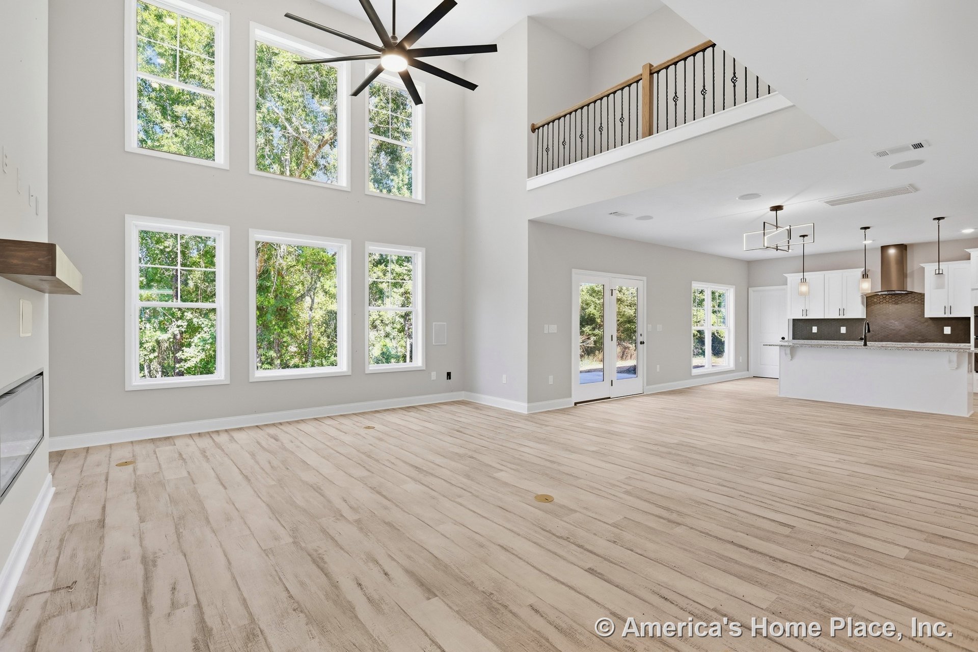 Double-height living area with expansive grid windows, modern ceiling fan, open kitchen featuring white cabinetry, granite countertops, tile backsplash, island with pendant