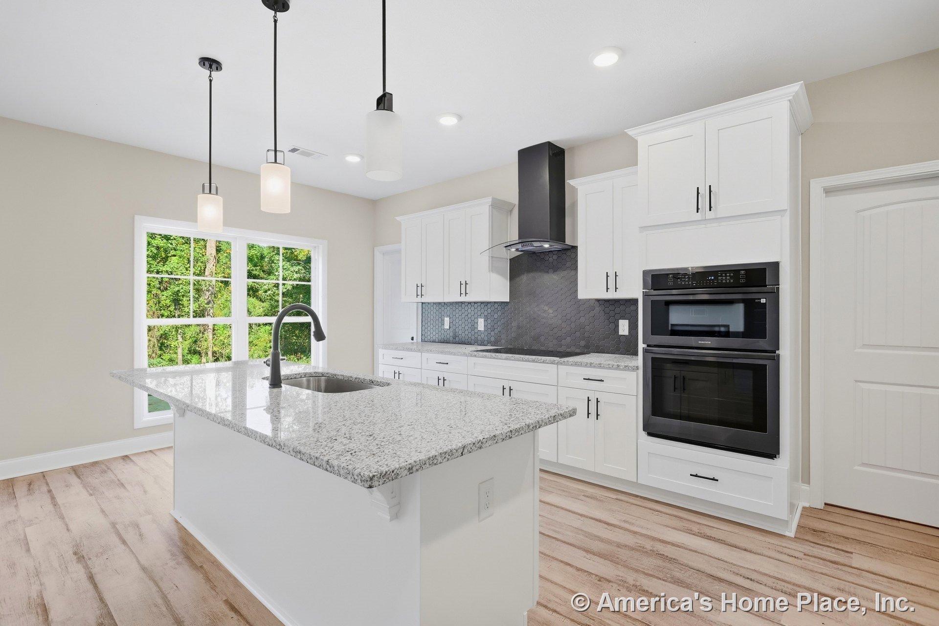 White kitchen with granite island featuring undermount sink, double wall ovens, hexagonal tile backsplash, large window with decorative trim, pendant and recessed lighting, and