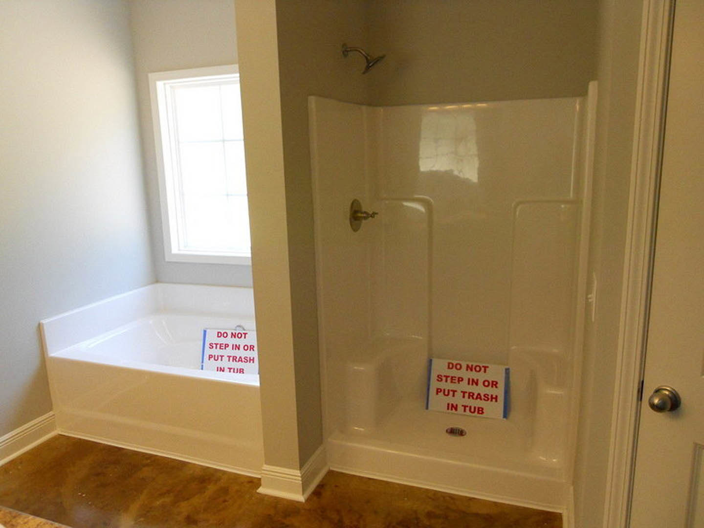 Bathroom with white tile shower, built-in tub, chrome door handle, and red sign displayed on shower wall.
