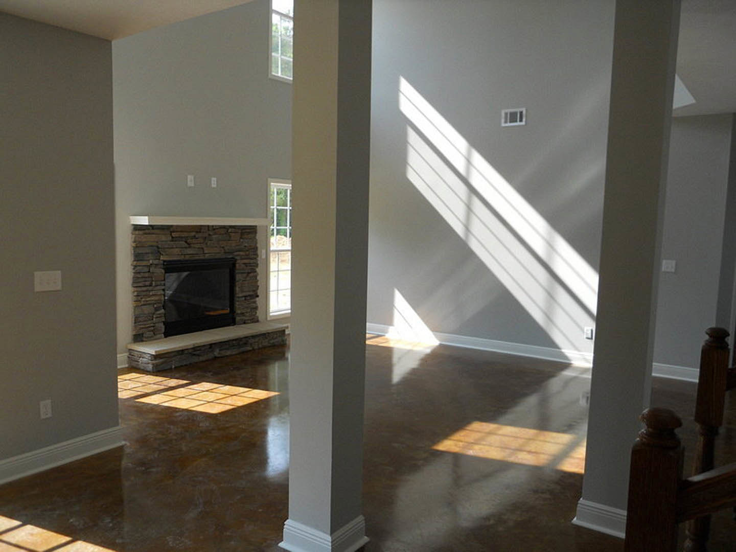 Living room with white pillars, stone fireplace, light wood flooring, large window with sunlight streaming in, plaster ceiling