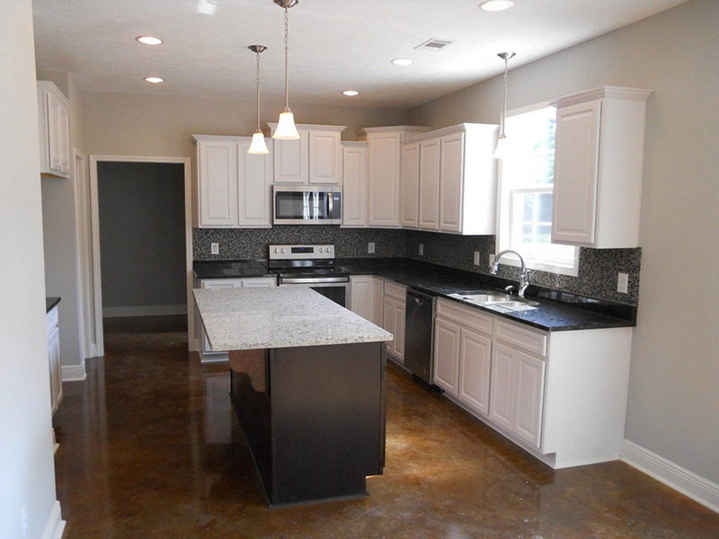 White cabinetry and black countertops in a modern kitchen with a central island, stainless steel faucet, and built-in appliances.
