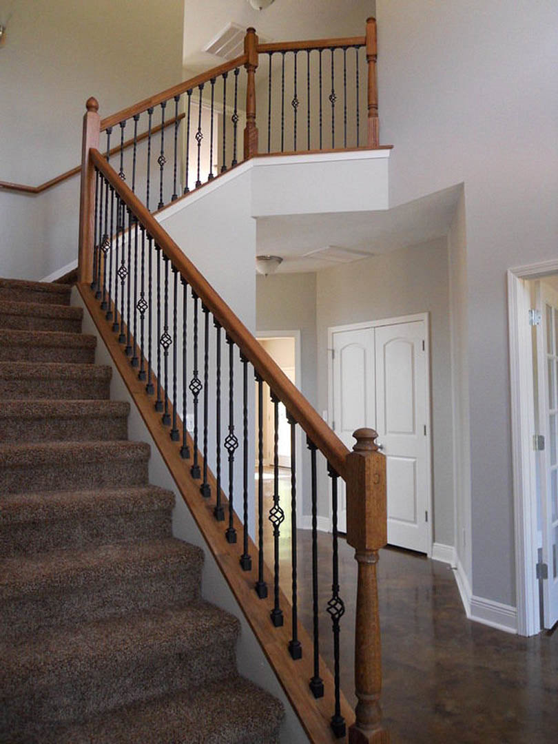 Curved staircase with black iron railings, wooden steps, and brown hardwood flooring adjacent to a white wall