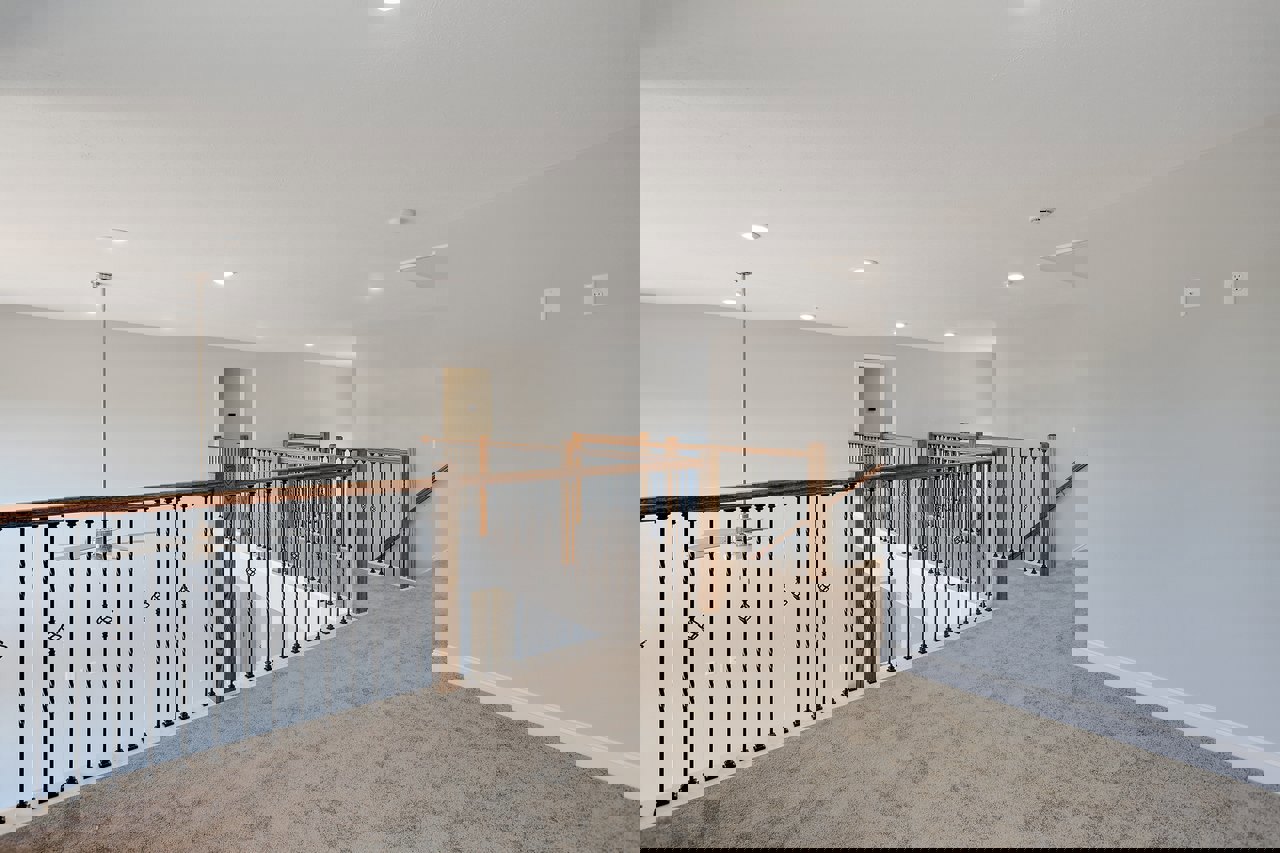 Carpeted staircase with wood railing and metal balusters, adjacent to a plaster wall featuring electrical outlets and a black rectangular device.