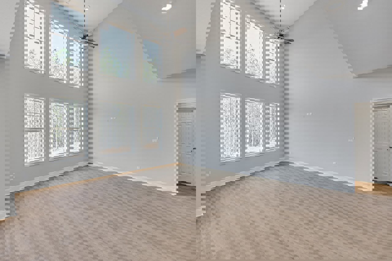 Spacious room featuring multiple large windows with views of trees, wood flooring, white door with silver knob, plaster walls, and ceiling fan