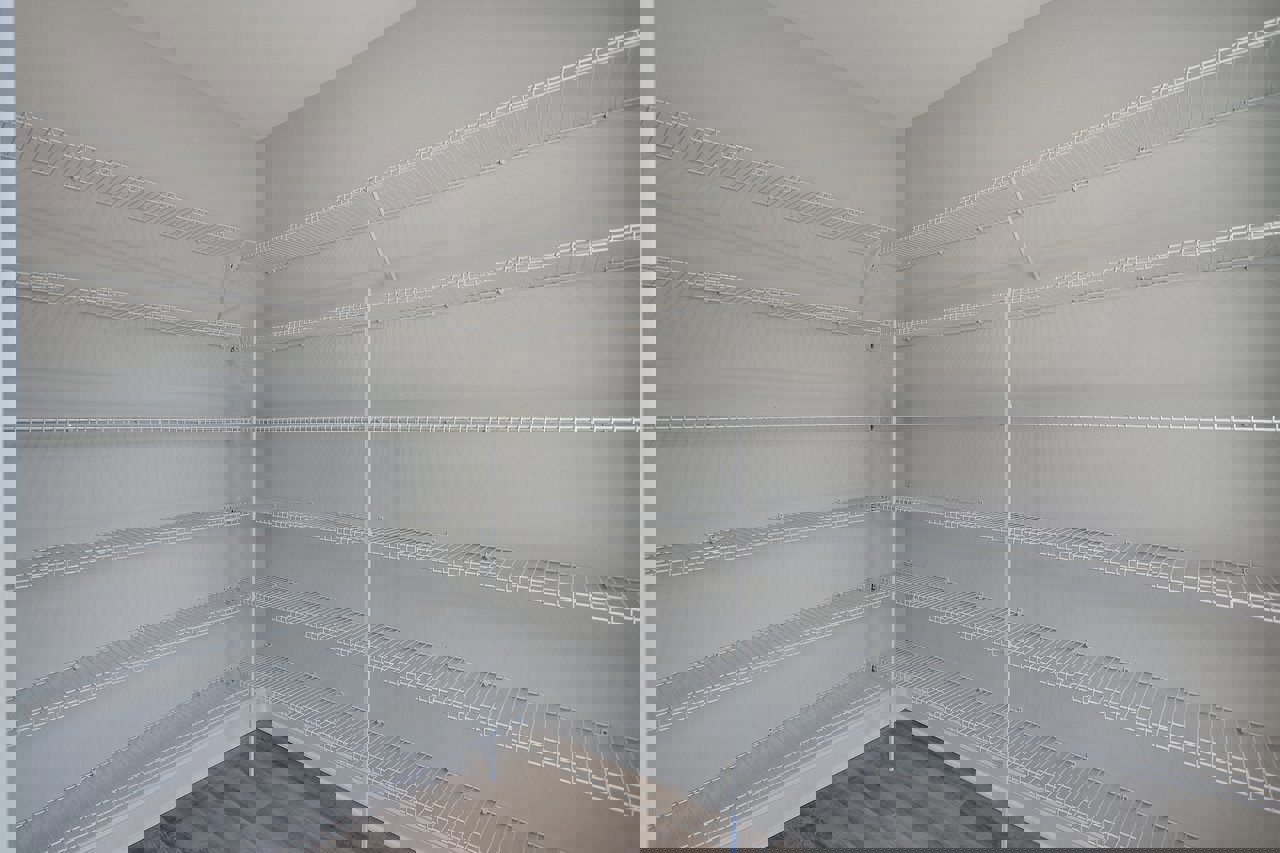 White built-in shelves and metal hanging rod in a closet with wood flooring and plaster walls