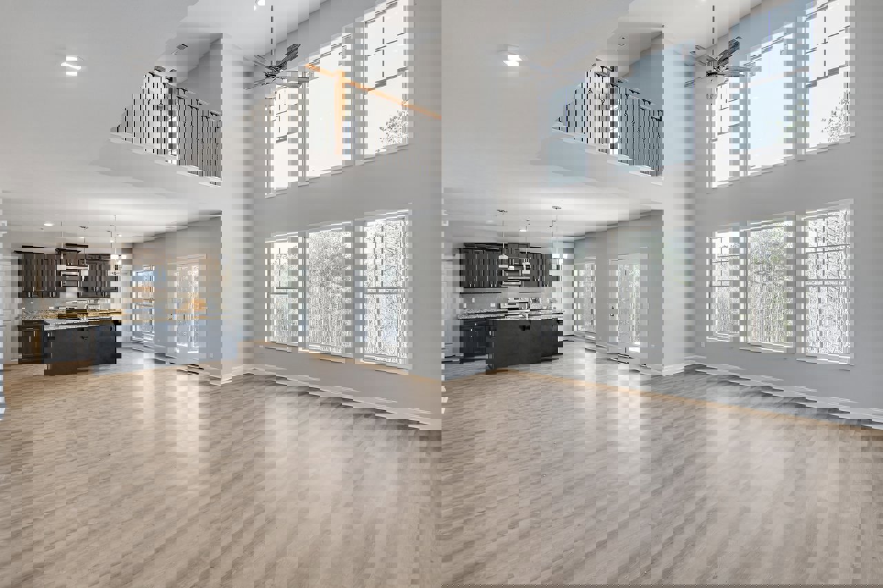 Open-concept kitchen with hardwood floors, large windows overlooking trees, black countertop with matching backsplash, ceiling fan with light fixture