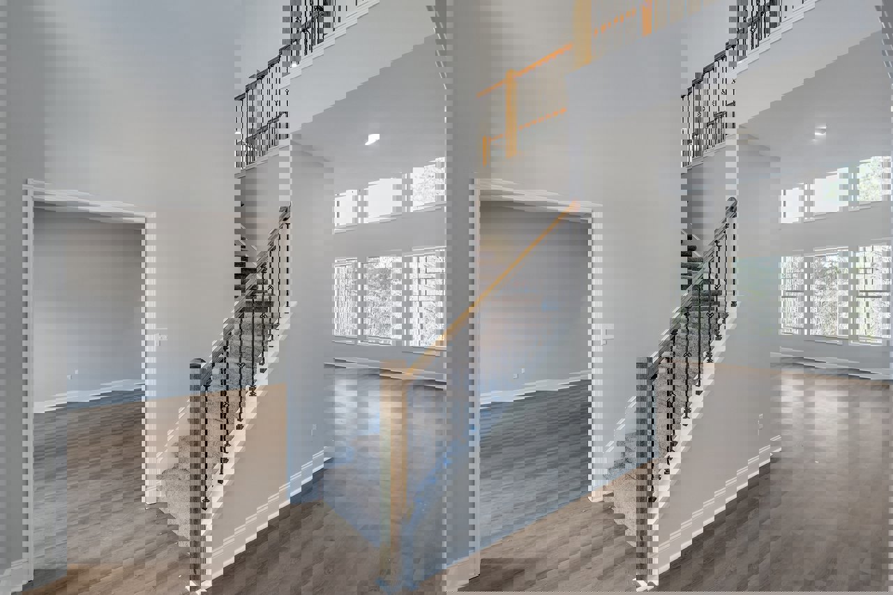 Wood staircase with metal railings, white plaster walls, large window with white frame overlooking trees, laminate wood flooring