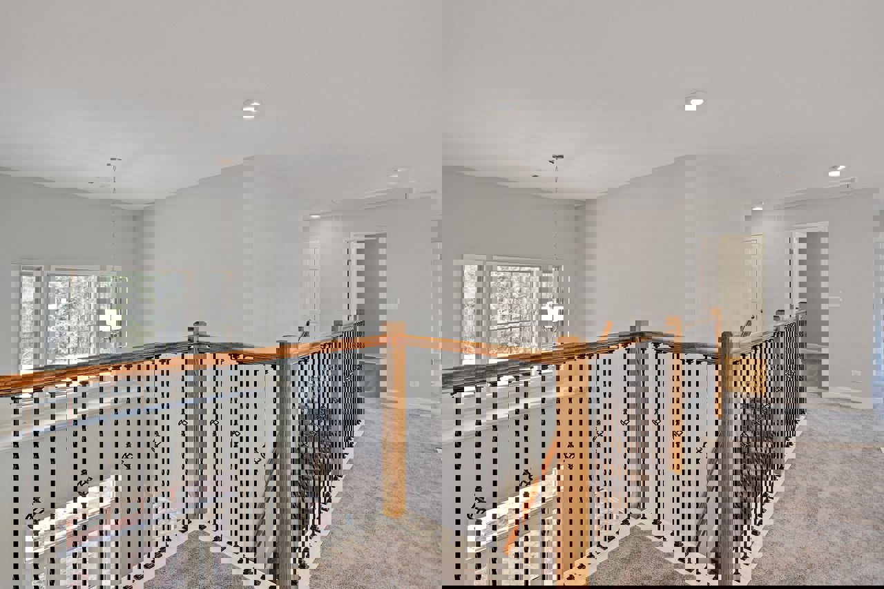 Wooden staircase with carpeted steps, white plaster walls, metal handrail, large window overlooking trees, recessed ceiling light