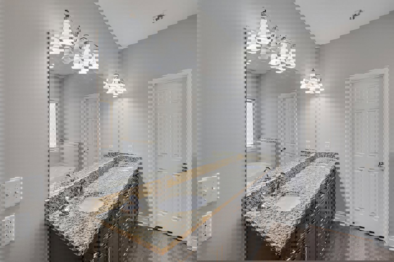 Bathroom with expansive marble countertop, undermount sink, chrome faucet, large wall mirror, white cabinetry, silver door knob, and dual light switches on white wall