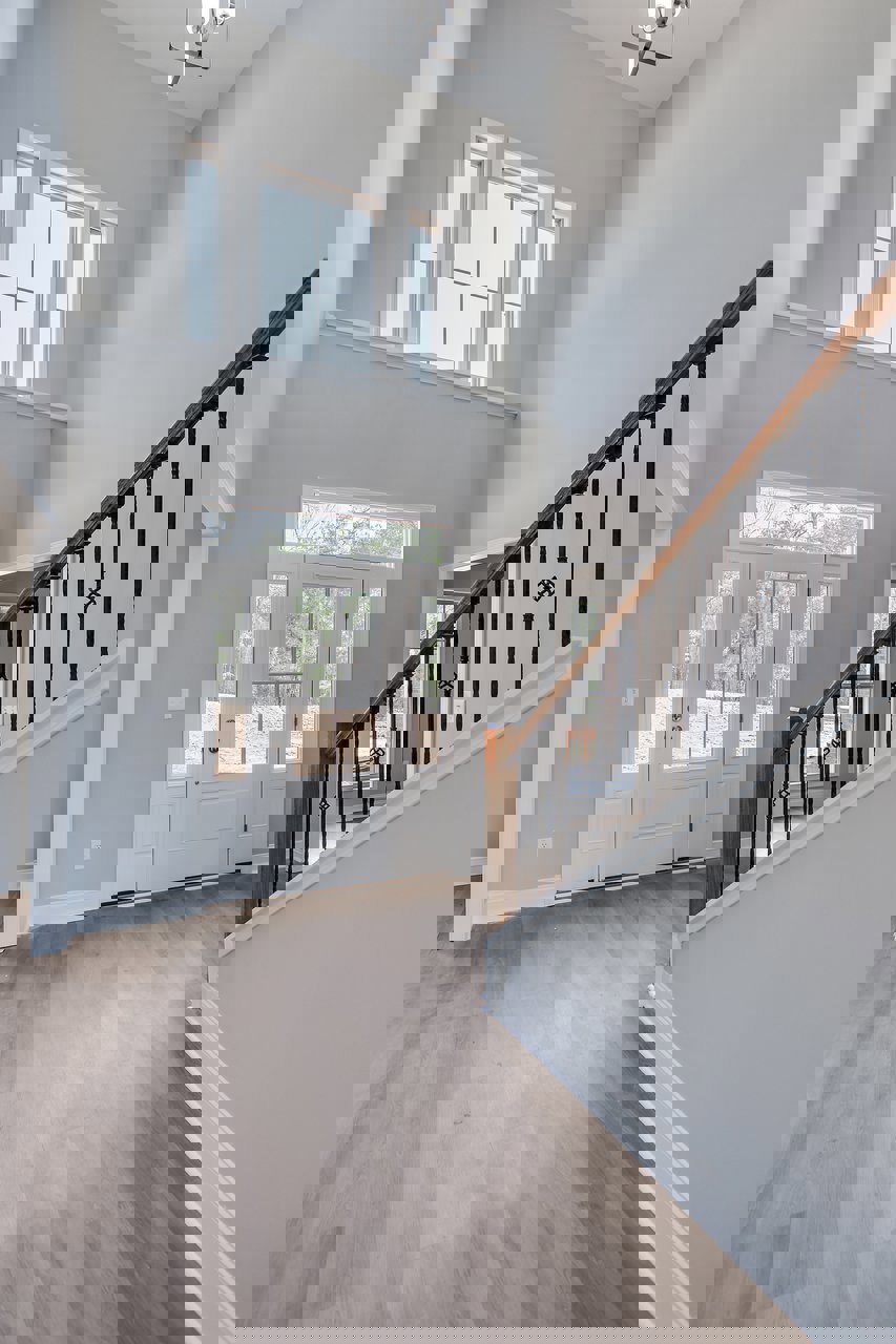 White staircase with black metal railings, laminate flooring, white door featuring glass panels, row of windows along plaster walls, modern light fixture overhead